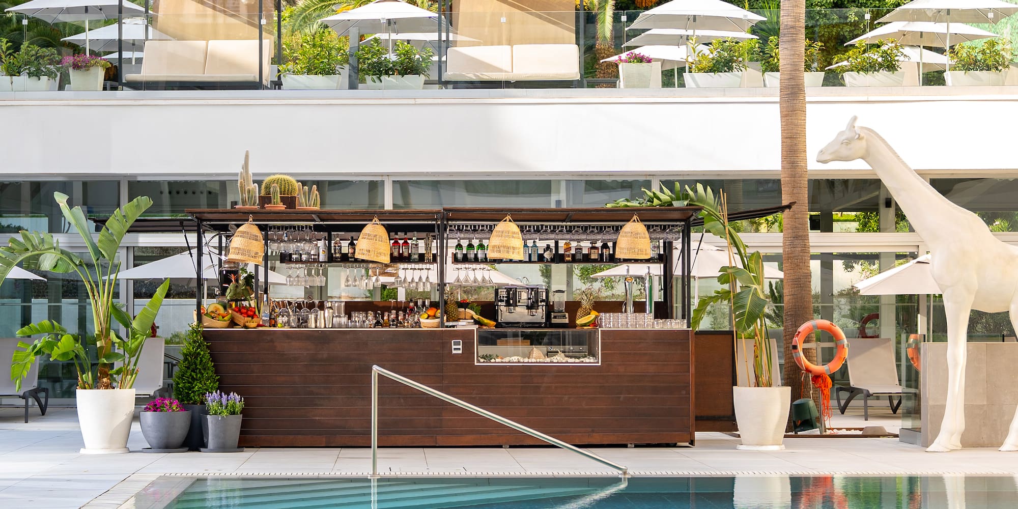 Luxury hotel pool bar with tropical plants, loungers, and giraffe statue.