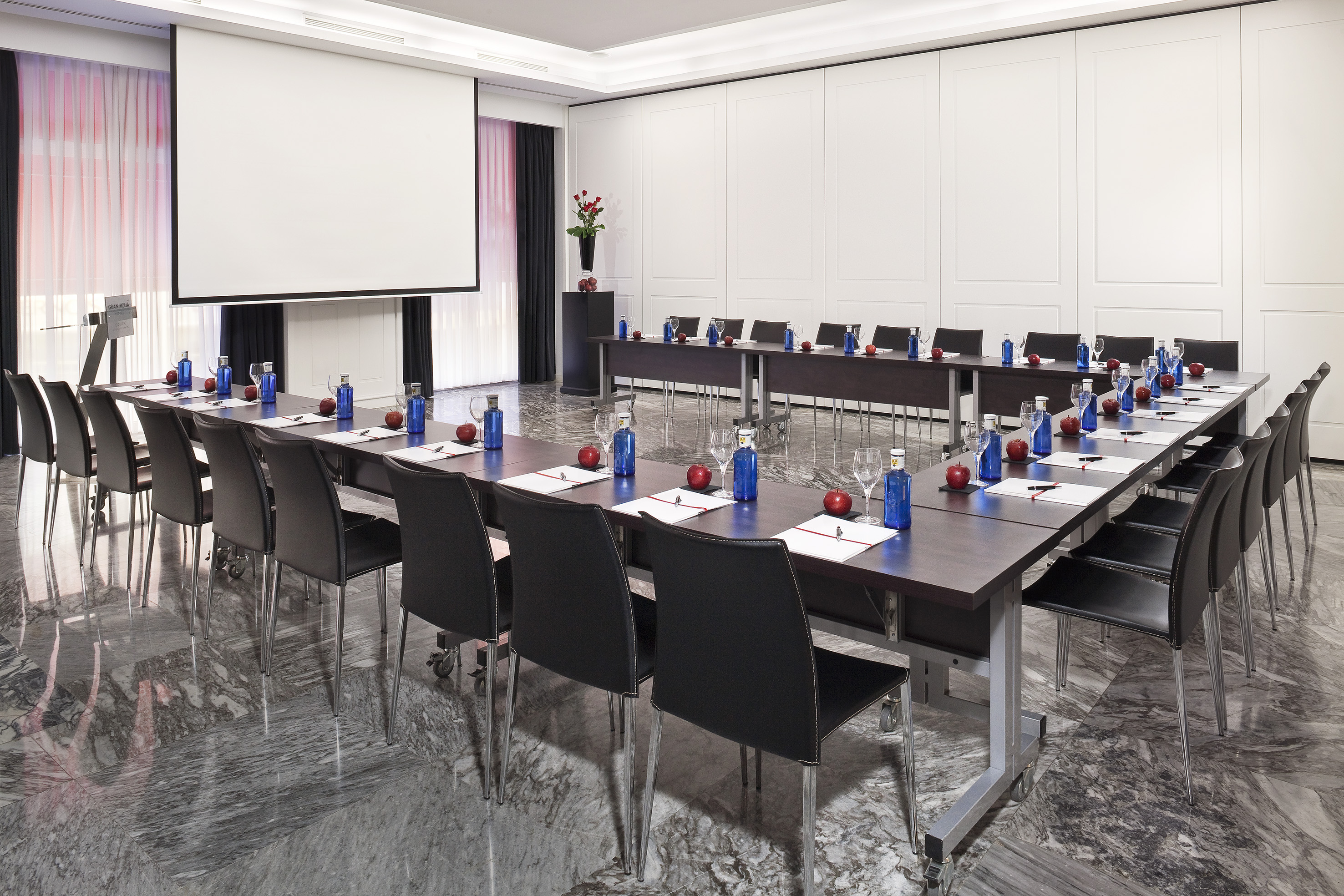 Modern conference room, U-shaped table, projector screen, professional setup.
