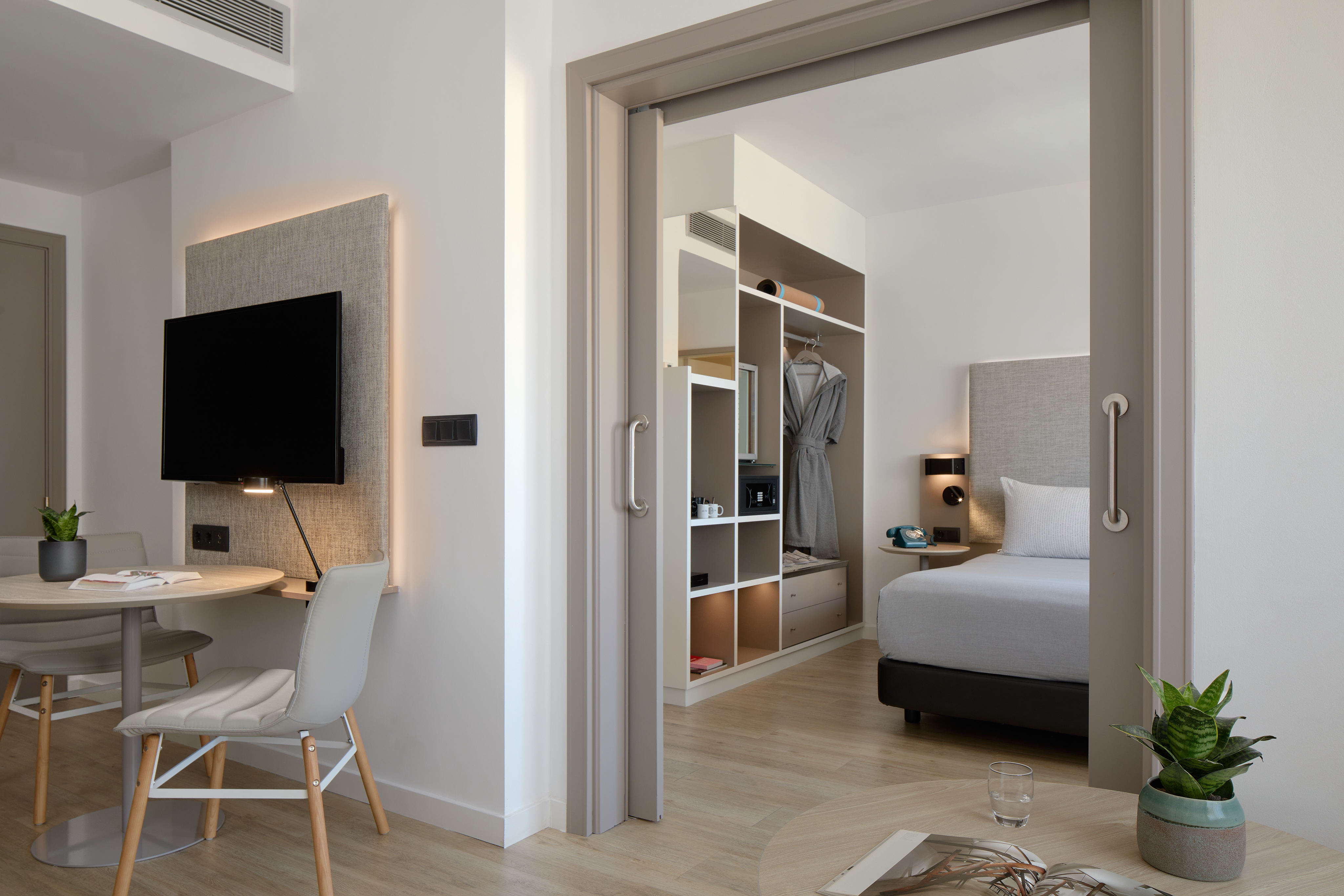 Modern hotel suite with desk, TV, and bedroom behind a sliding door.