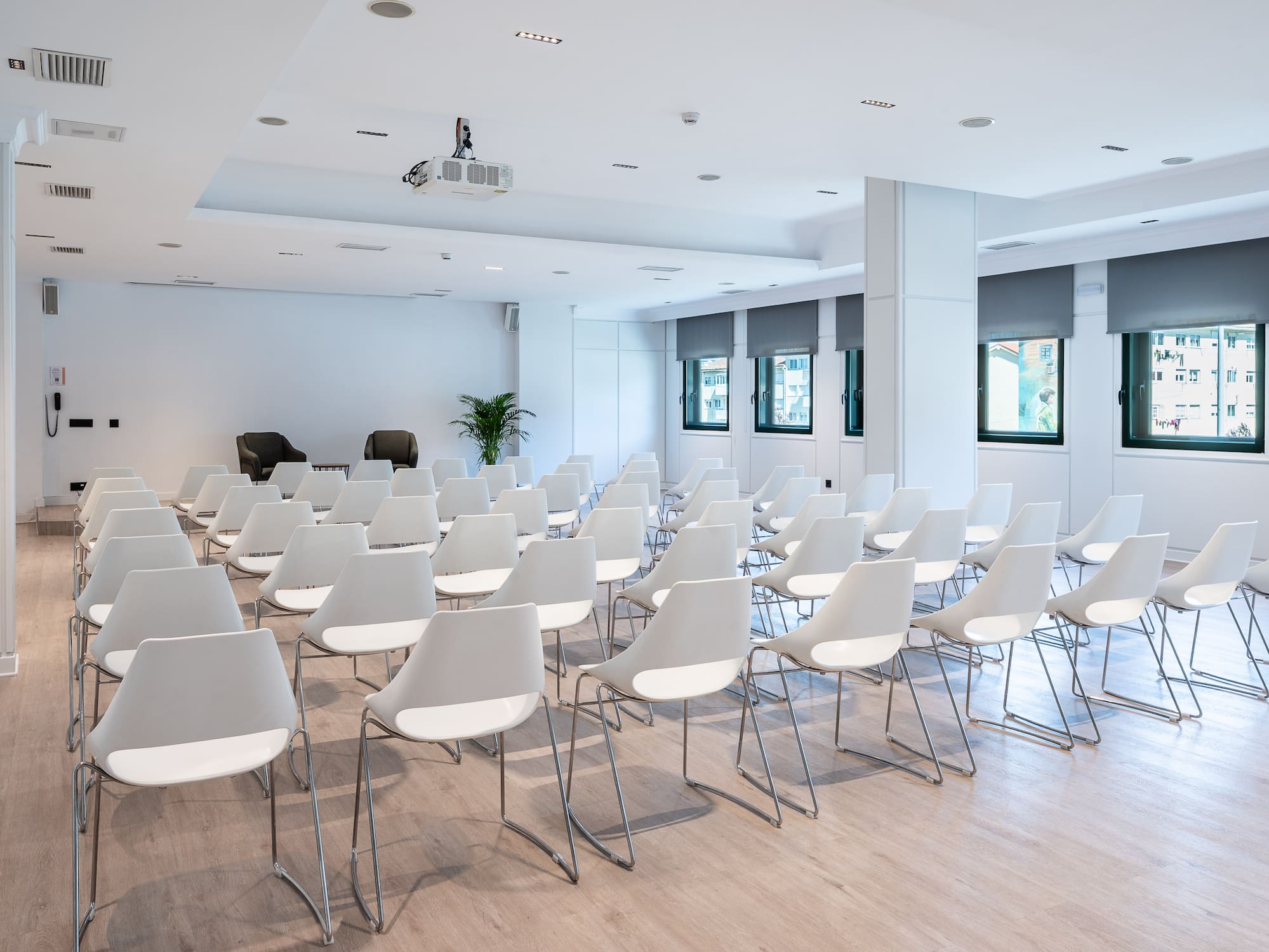 Modern meeting room with white chairs, projector, light floor, and large windows.