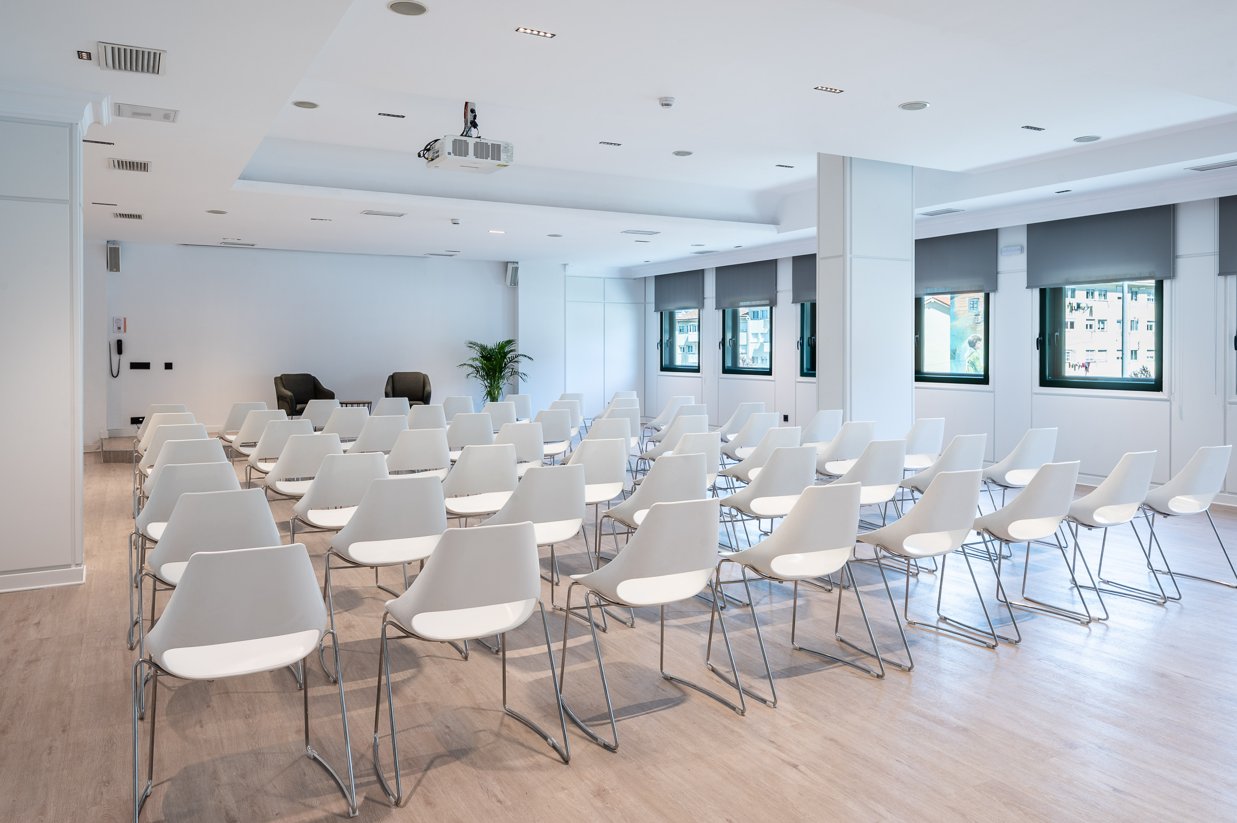 Modern meeting room with white chairs, projector, light floor, and large windows.