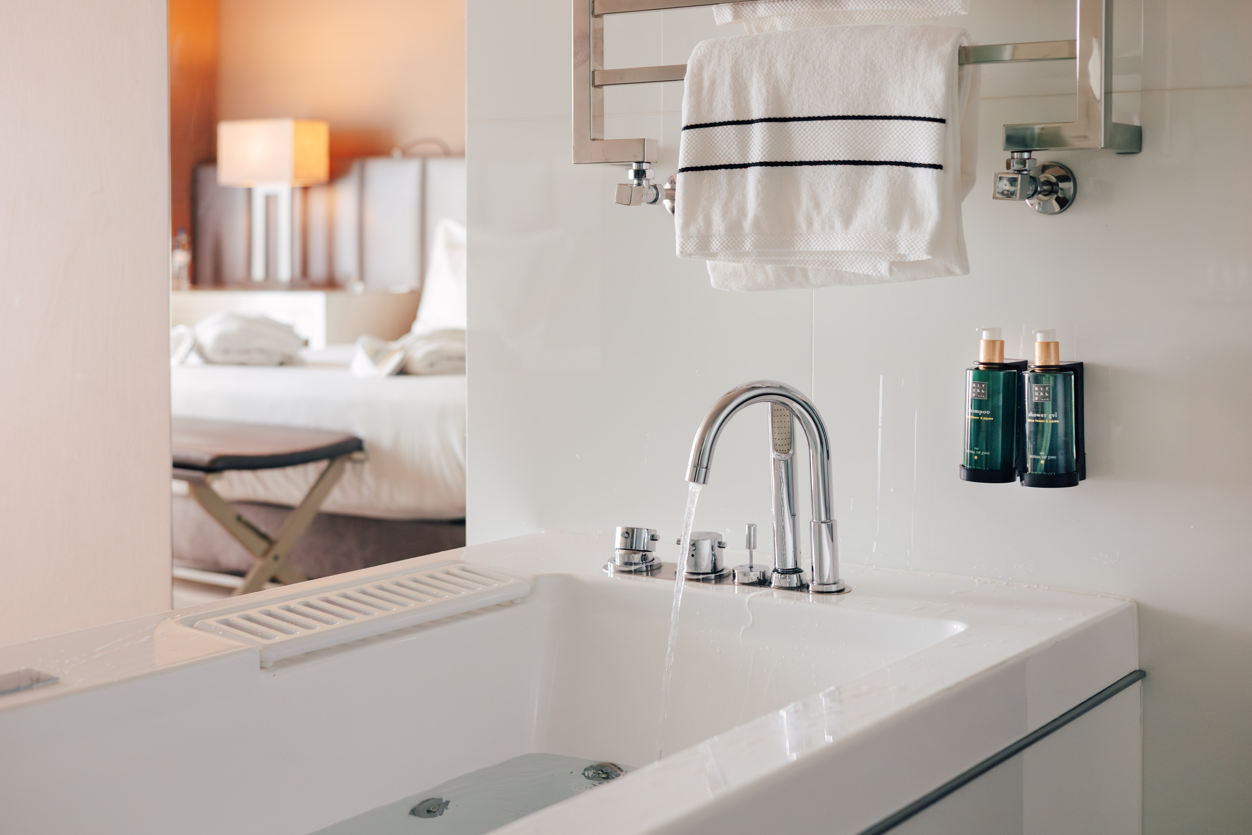 Modern hotel bathroom with bathtub, running water, towels, and amenities.