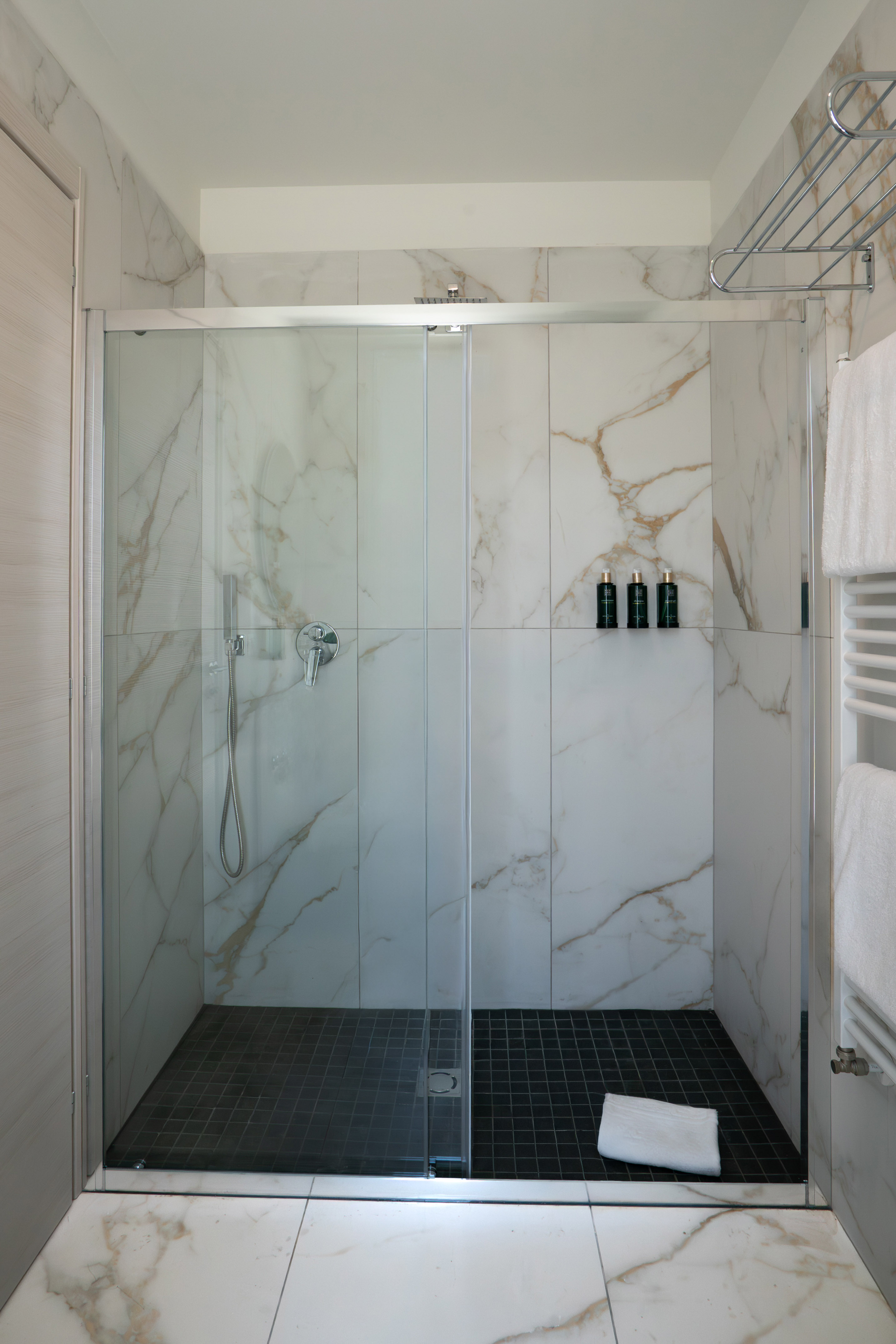 Modern marble-tiled shower with glass enclosure, dark floor, chrome fixtures.