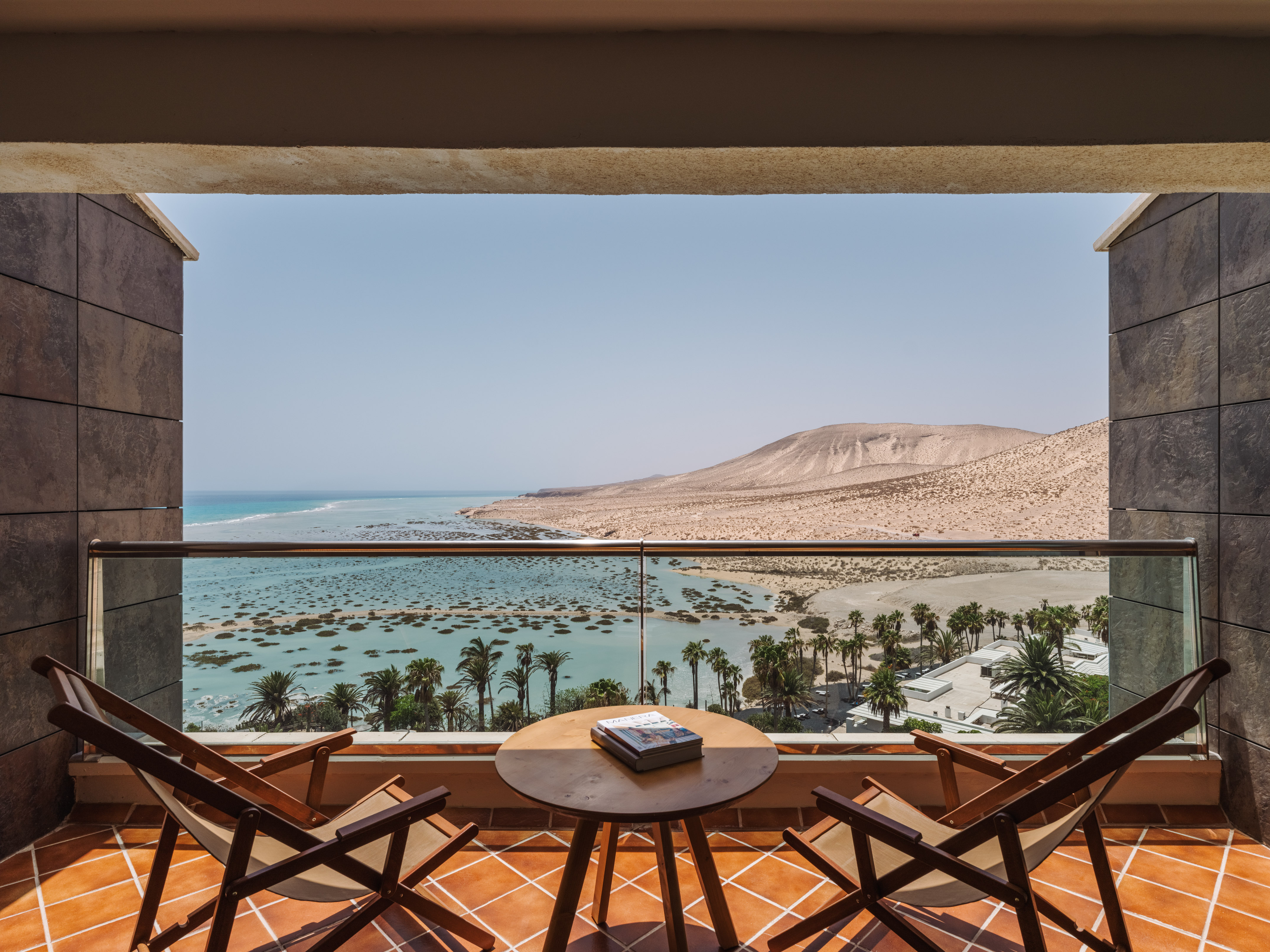 Resort balcony view: ocean lagoon, palm trees, desert landscape.