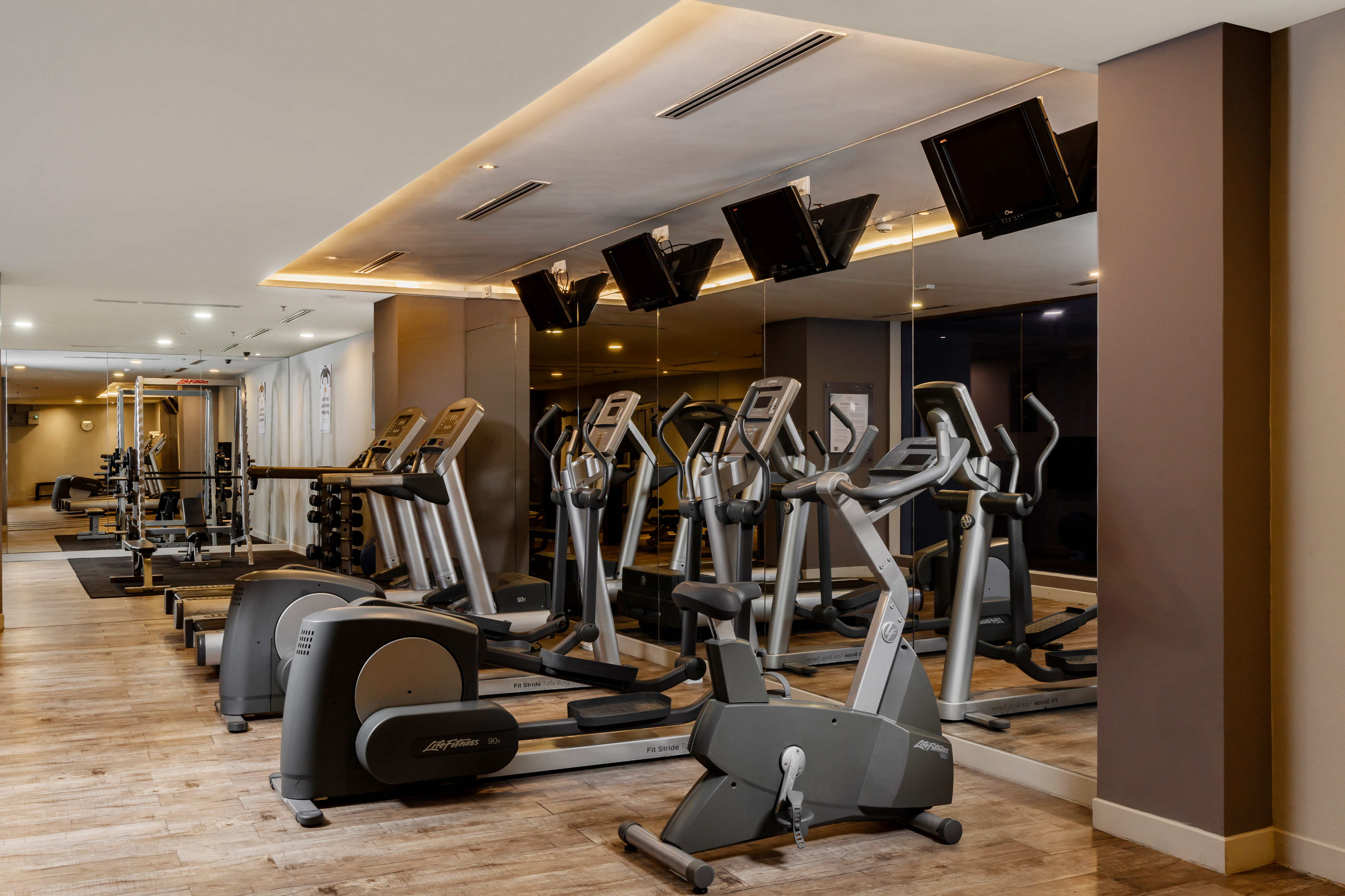 Bright gym interior with rows of cardio machines, ellipticals, and treadmills.