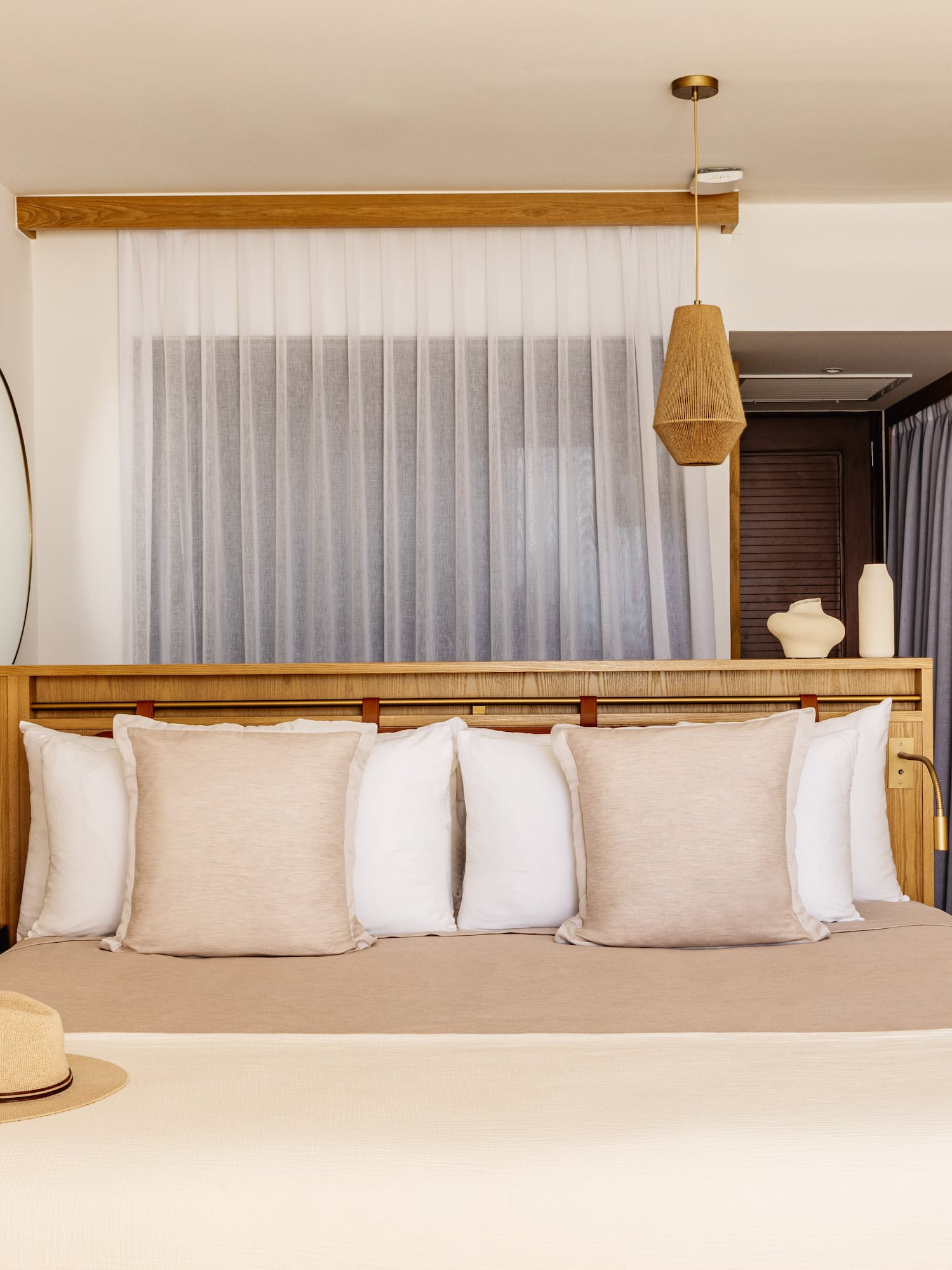 Neutral modern hotel bedroom with wooden headboard, macrame, and rattan decor.