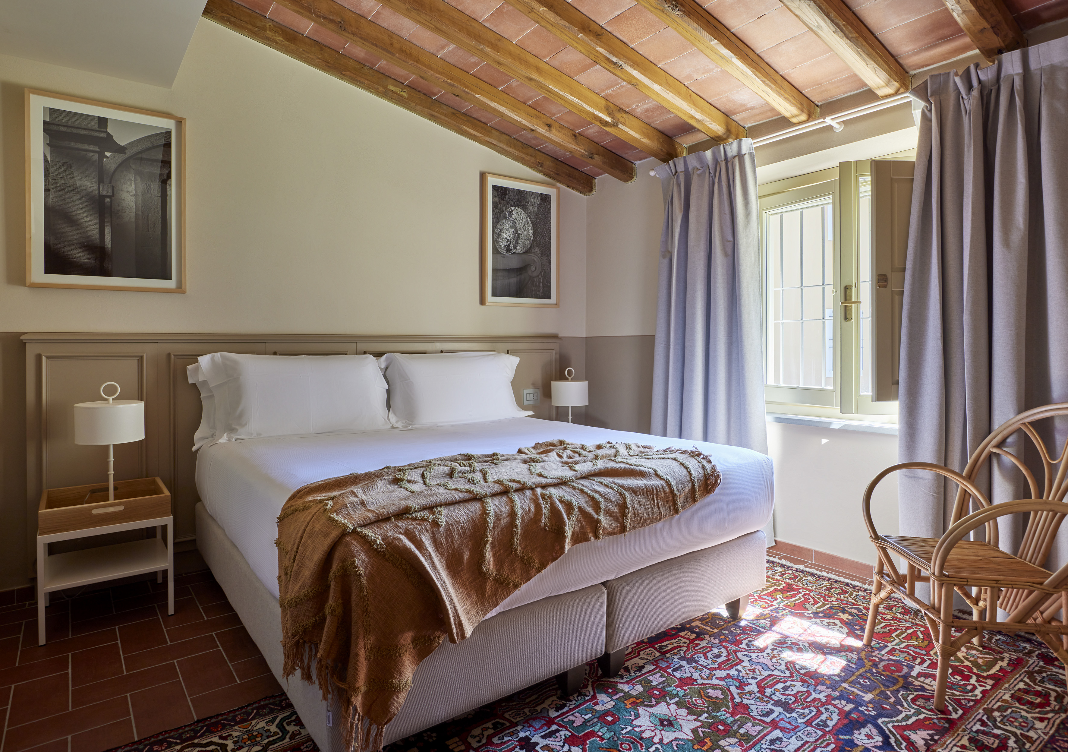 Rustic hotel bedroom with exposed beams, terracotta ceiling, and patterned rug.
