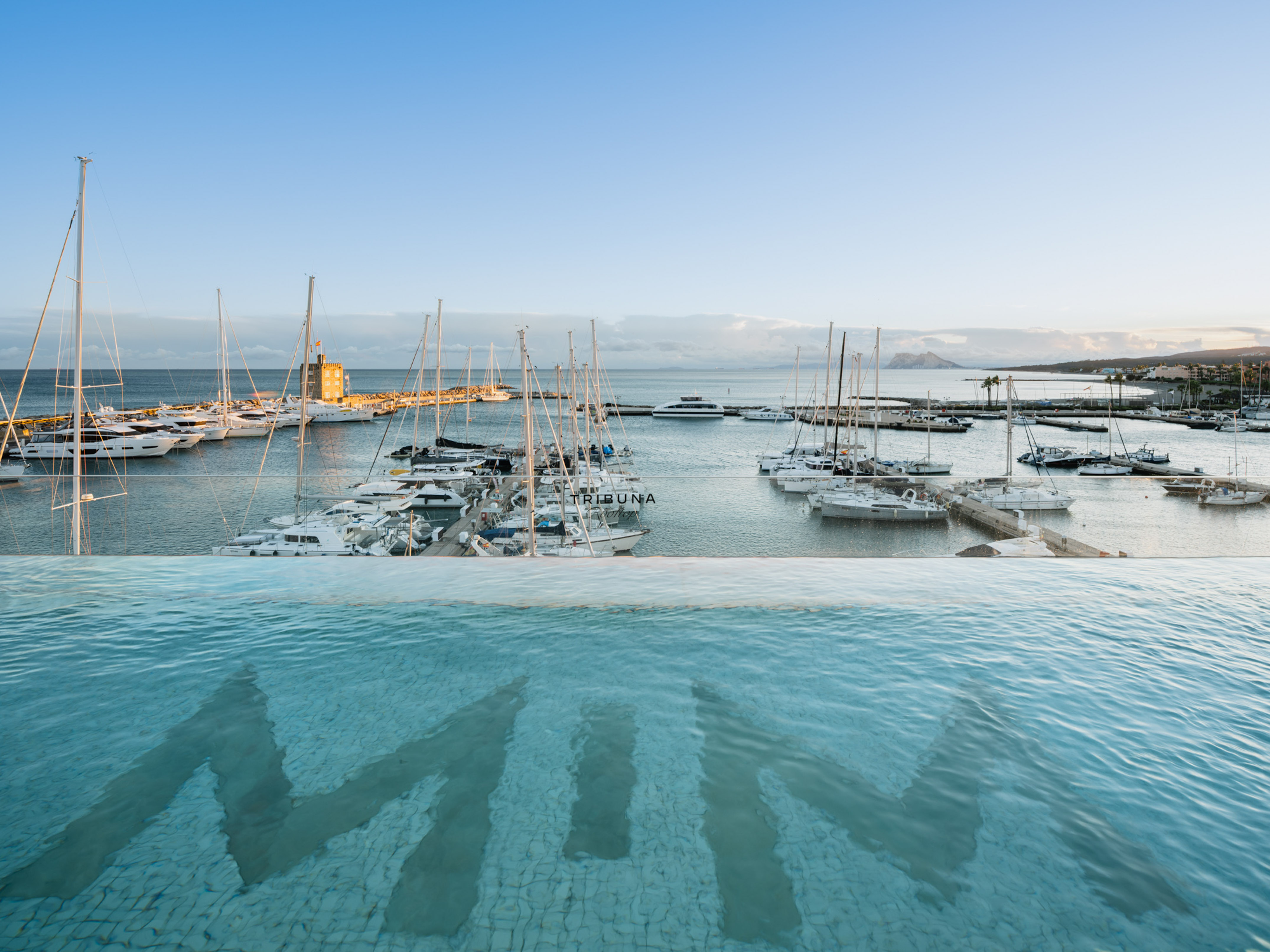 Infinity pool with 'MIN' logo overlooking marina with yachts and boats.