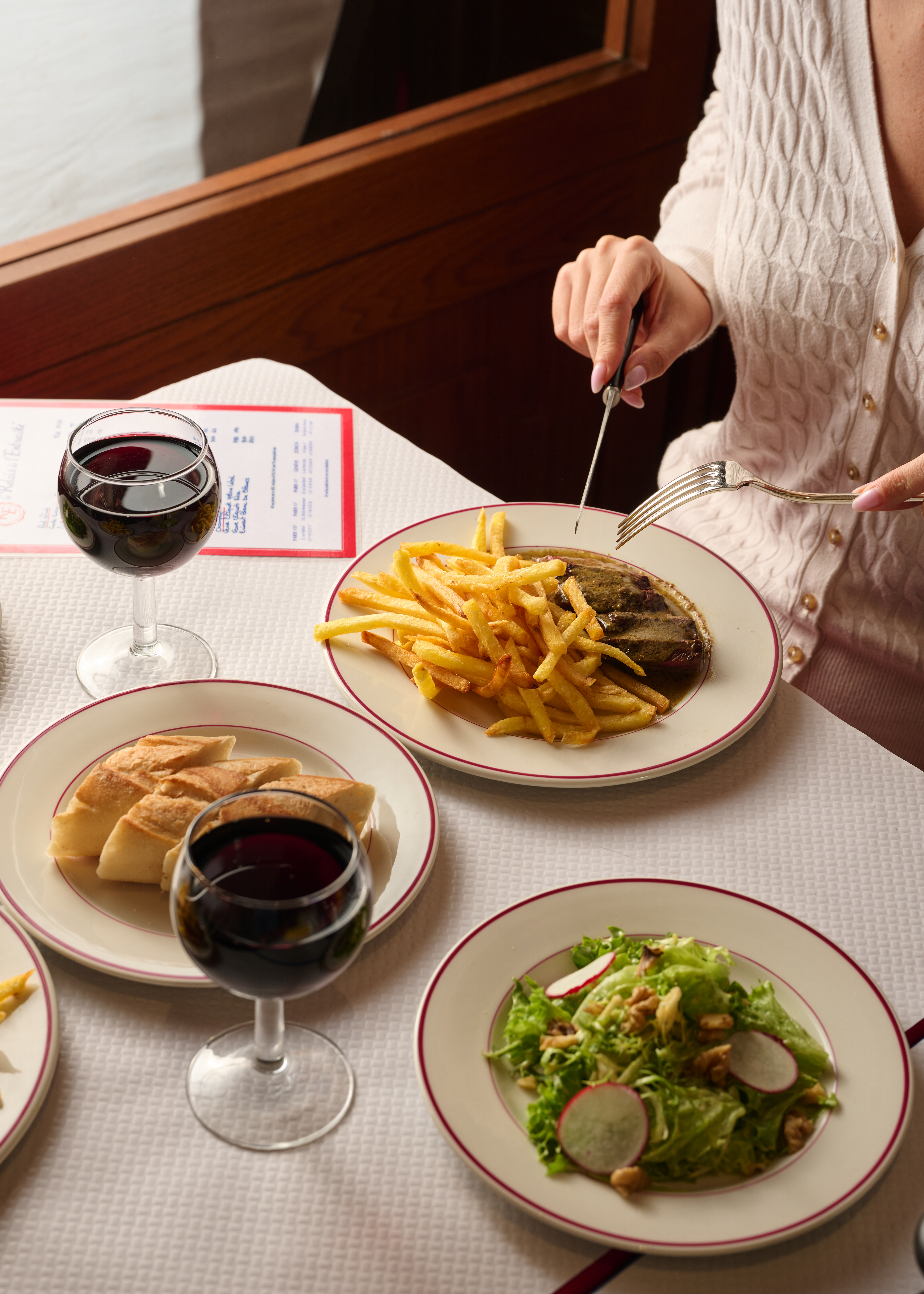 Steak frites meal with red wine, bread, and salad at a bistro table.