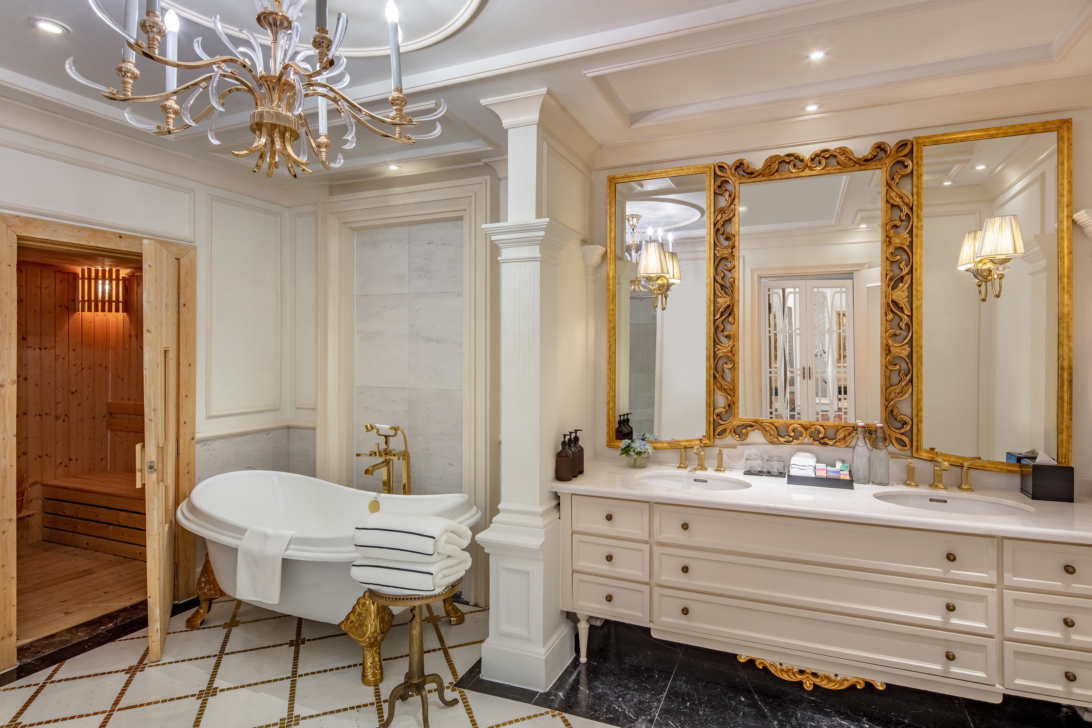 Luxury bathroom with freestanding bathtub, dual vanity, gold mirror, and sauna.