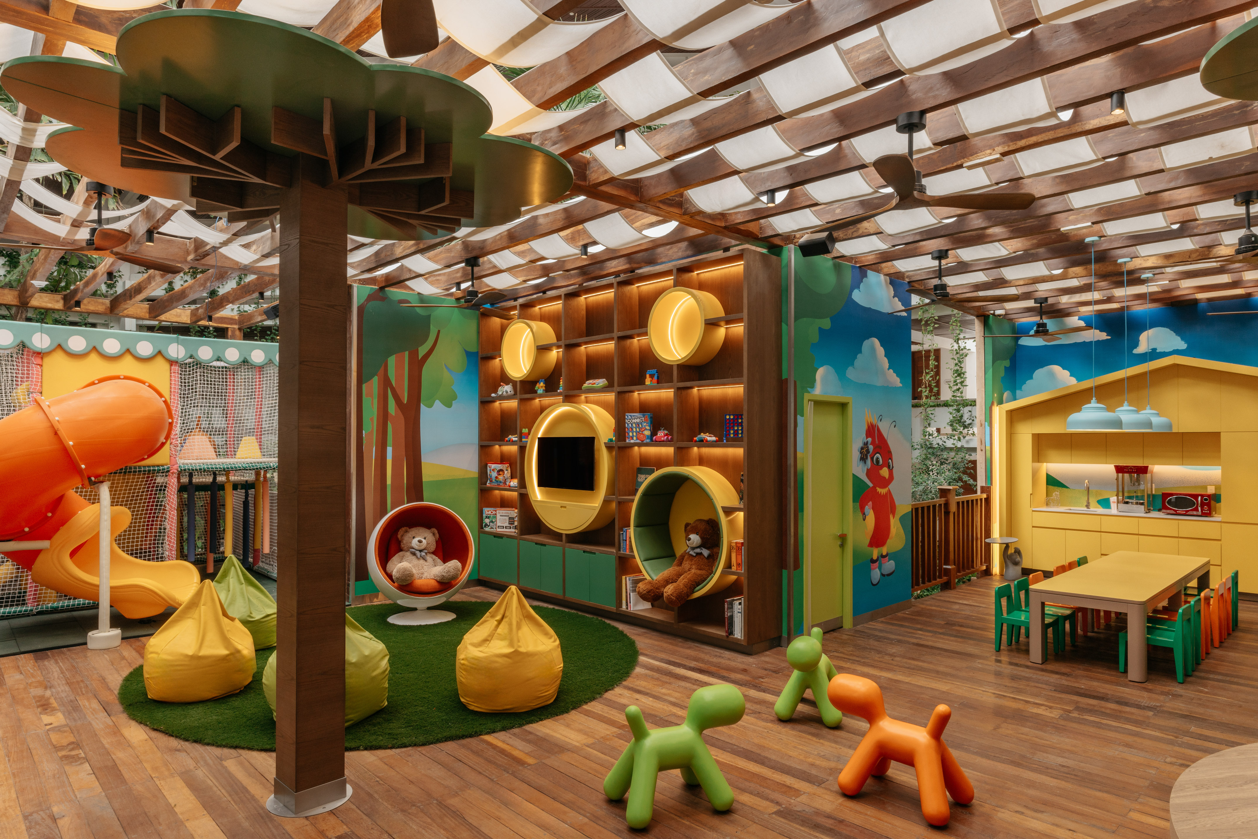 Colorful indoor kids' playroom with slide, tree column, activity wall, and seating.