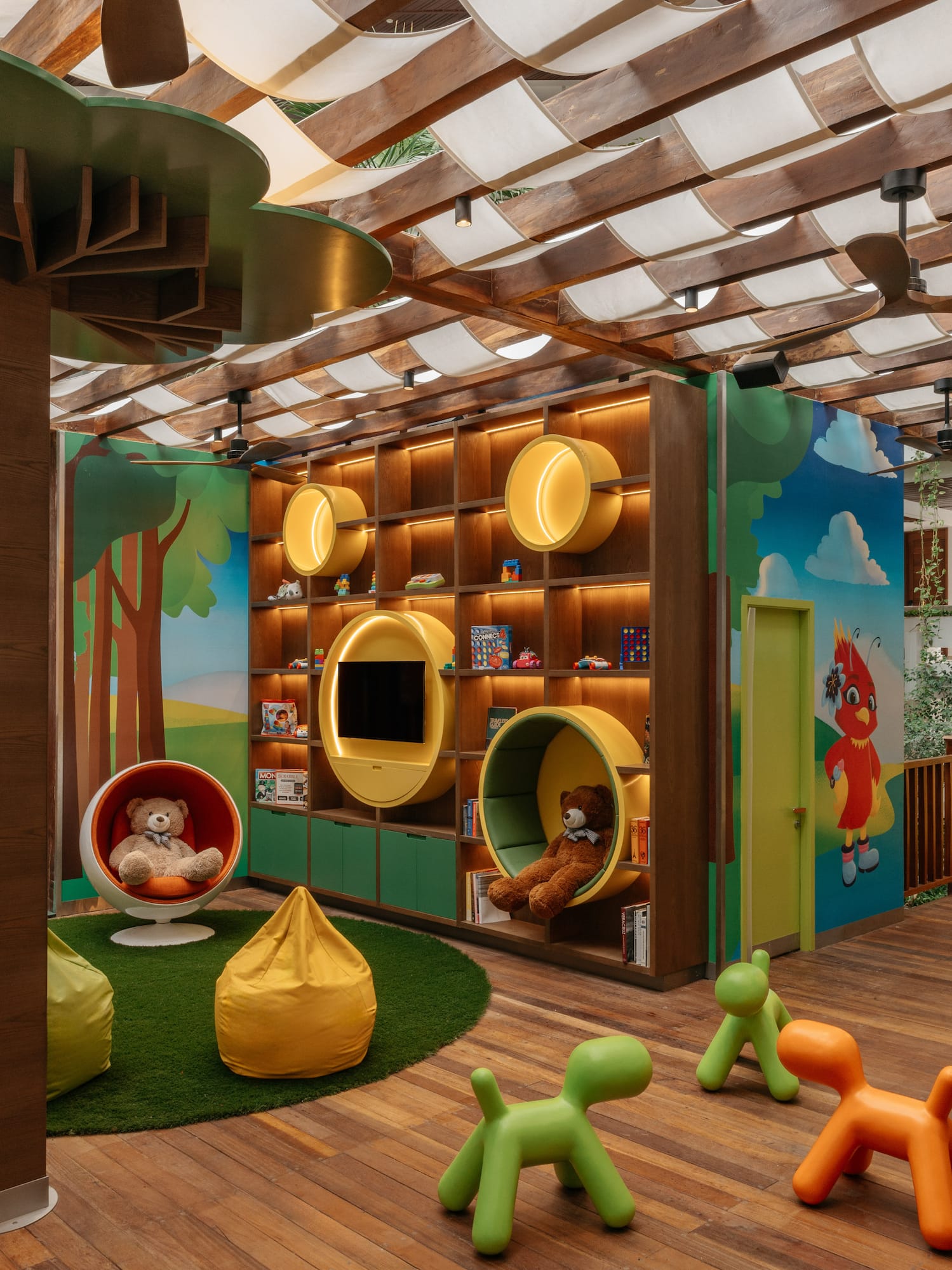 Colorful indoor kids' playroom with slide, tree column, activity wall, and seating.