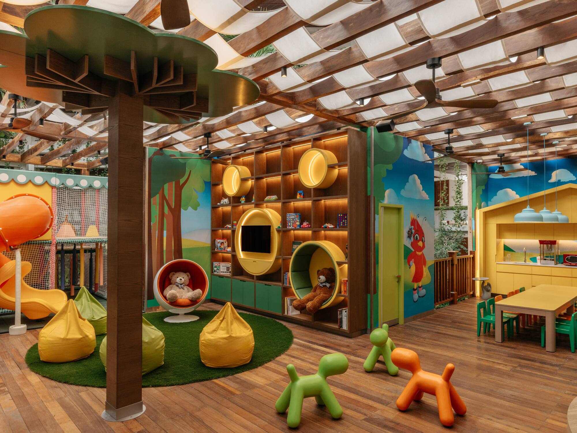 Colorful indoor kids' playroom with slide, tree column, activity wall, and seating.