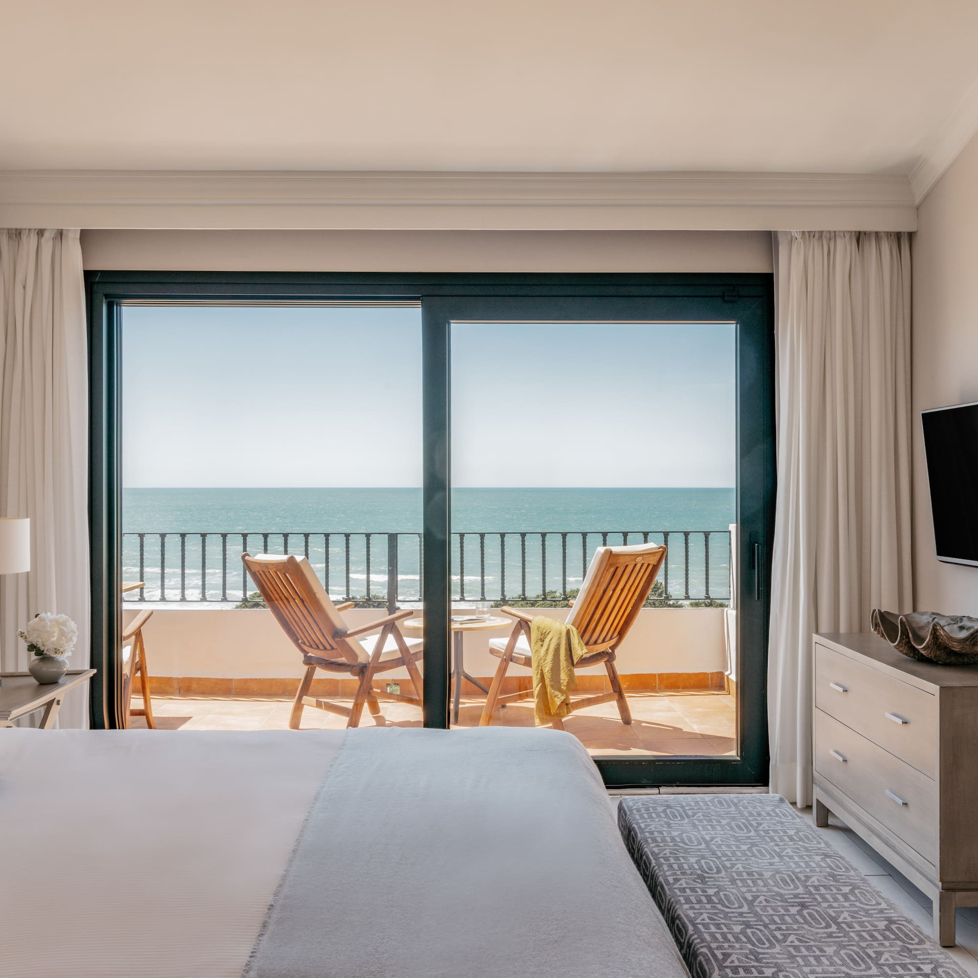 Bedroom with ocean view balcony, two chairs, and a bed in a luxury hotel.