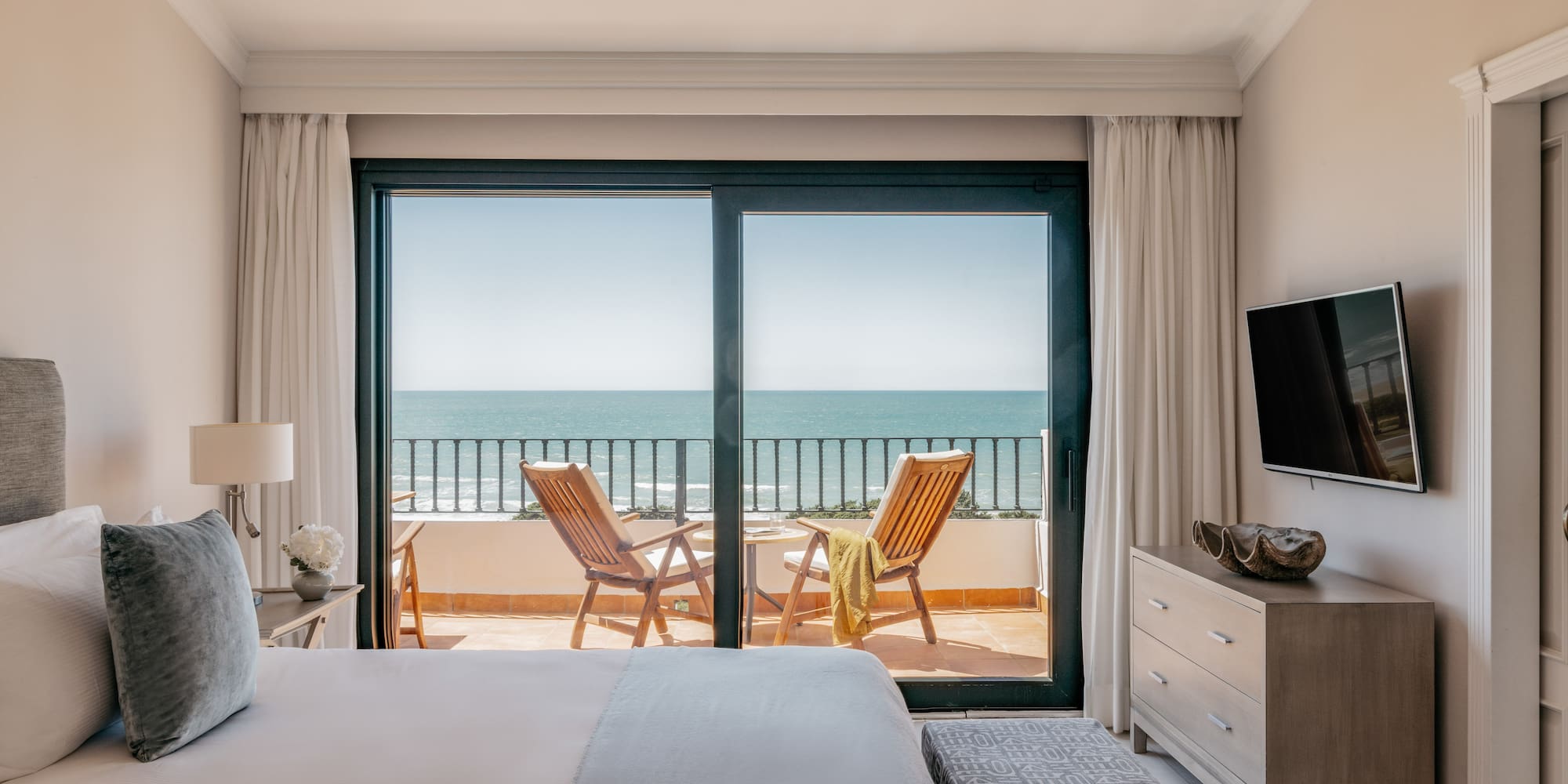 Bedroom with ocean view balcony, two chairs, and a bed in a luxury hotel.