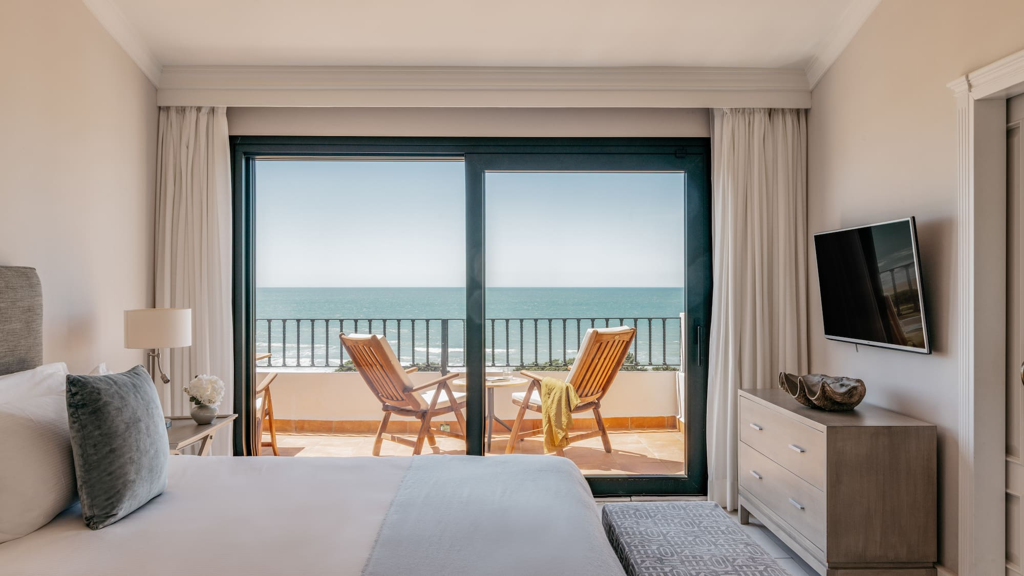 Bedroom with ocean view balcony, two chairs, and a bed in a luxury hotel.