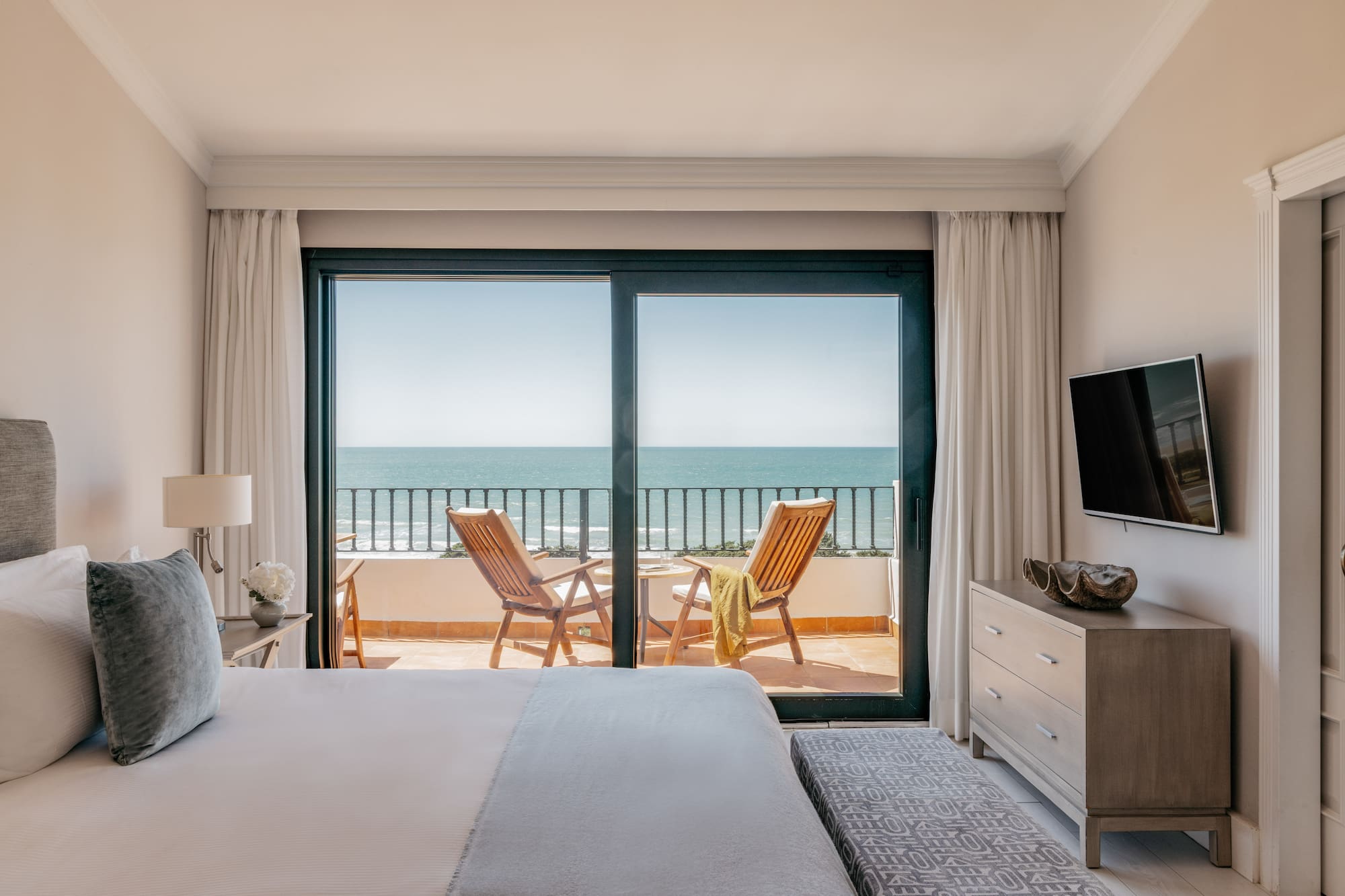 Bedroom with ocean view balcony, two chairs, and a bed in a luxury hotel.