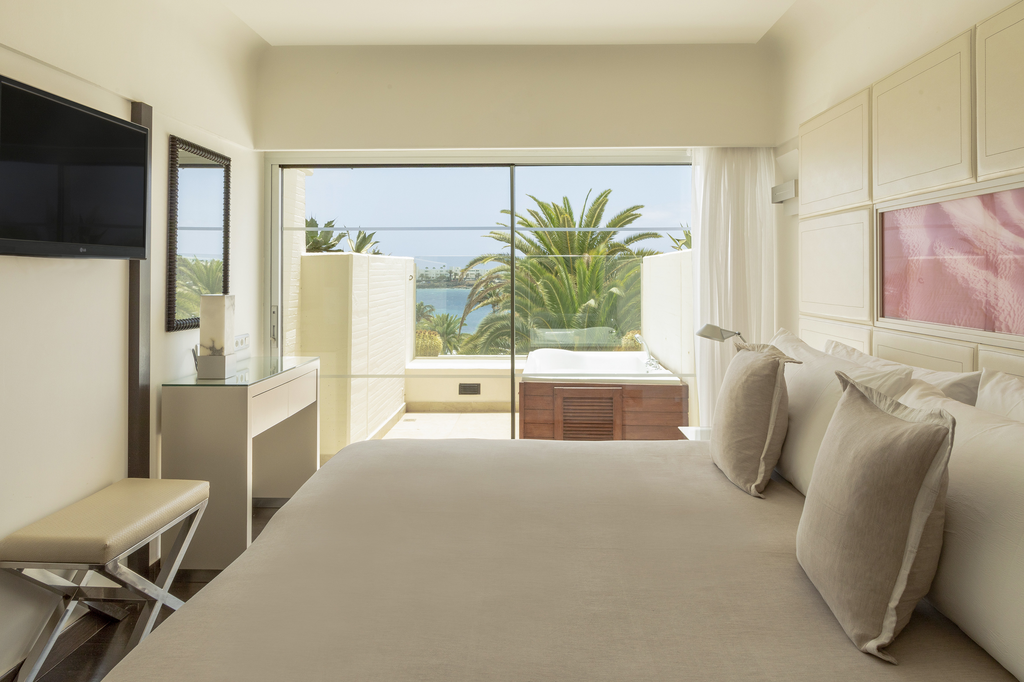 Hotel room with sea view, private balcony hot tub, and lush palm trees.