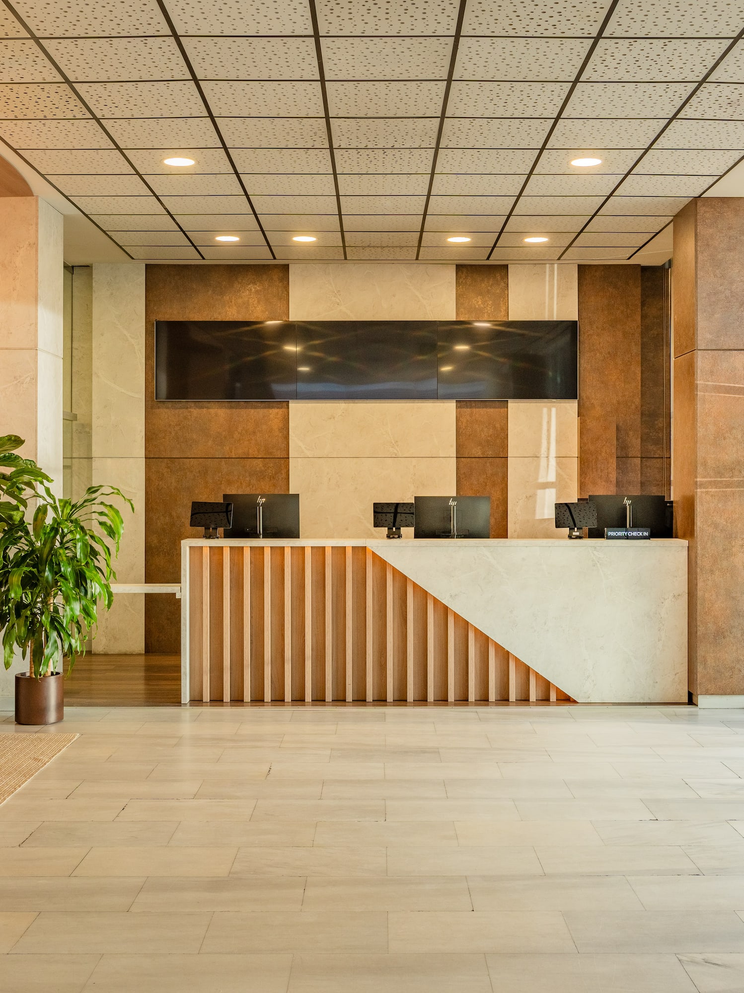 Modern hotel reception with wood and marble desk, green plants, glass doors.