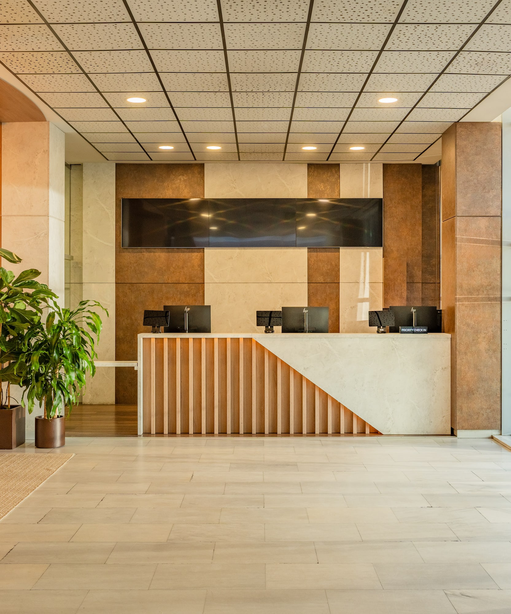 Modern hotel reception with wood and marble desk, green plants, glass doors.