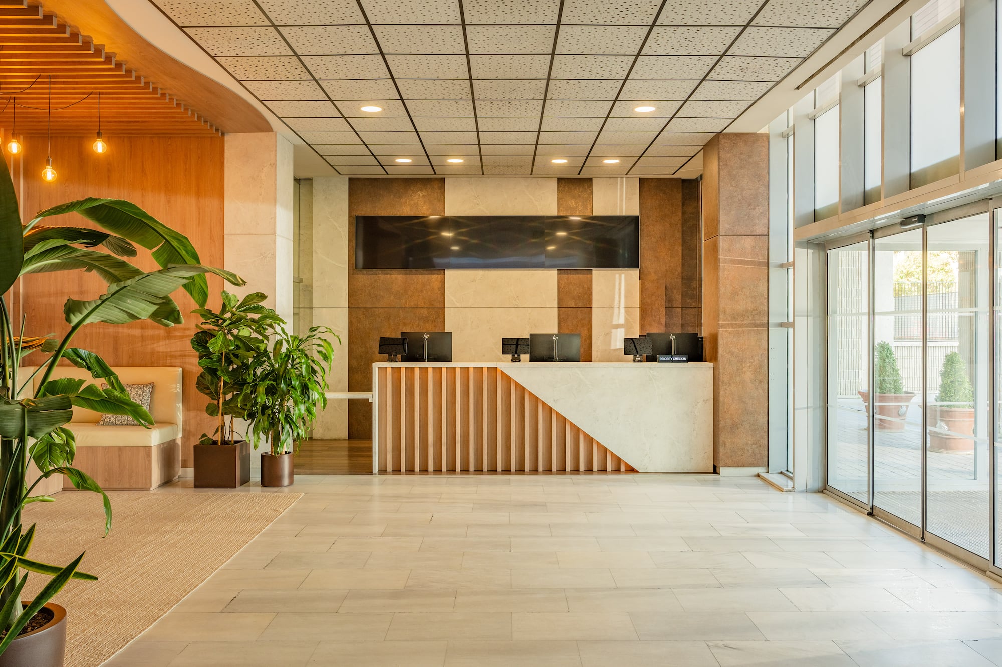 Modern hotel lobby with reception desk, green plants, and bright glass entrance.