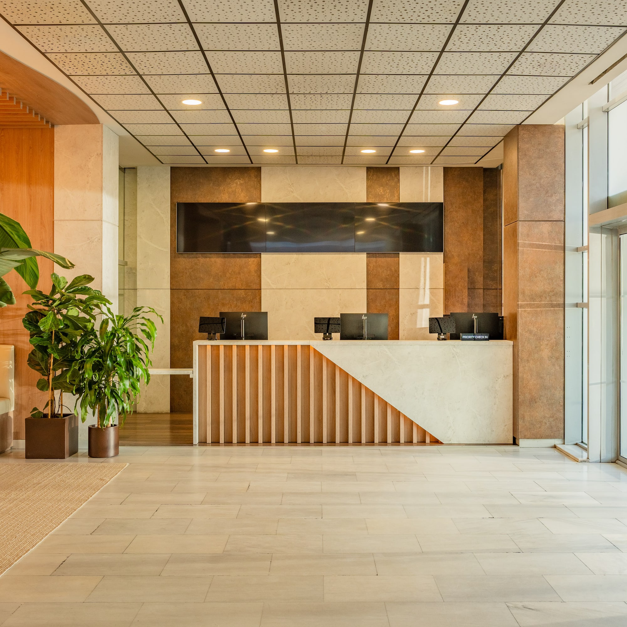 Modern hotel lobby with reception desk, plants, wood accents, glass doors.