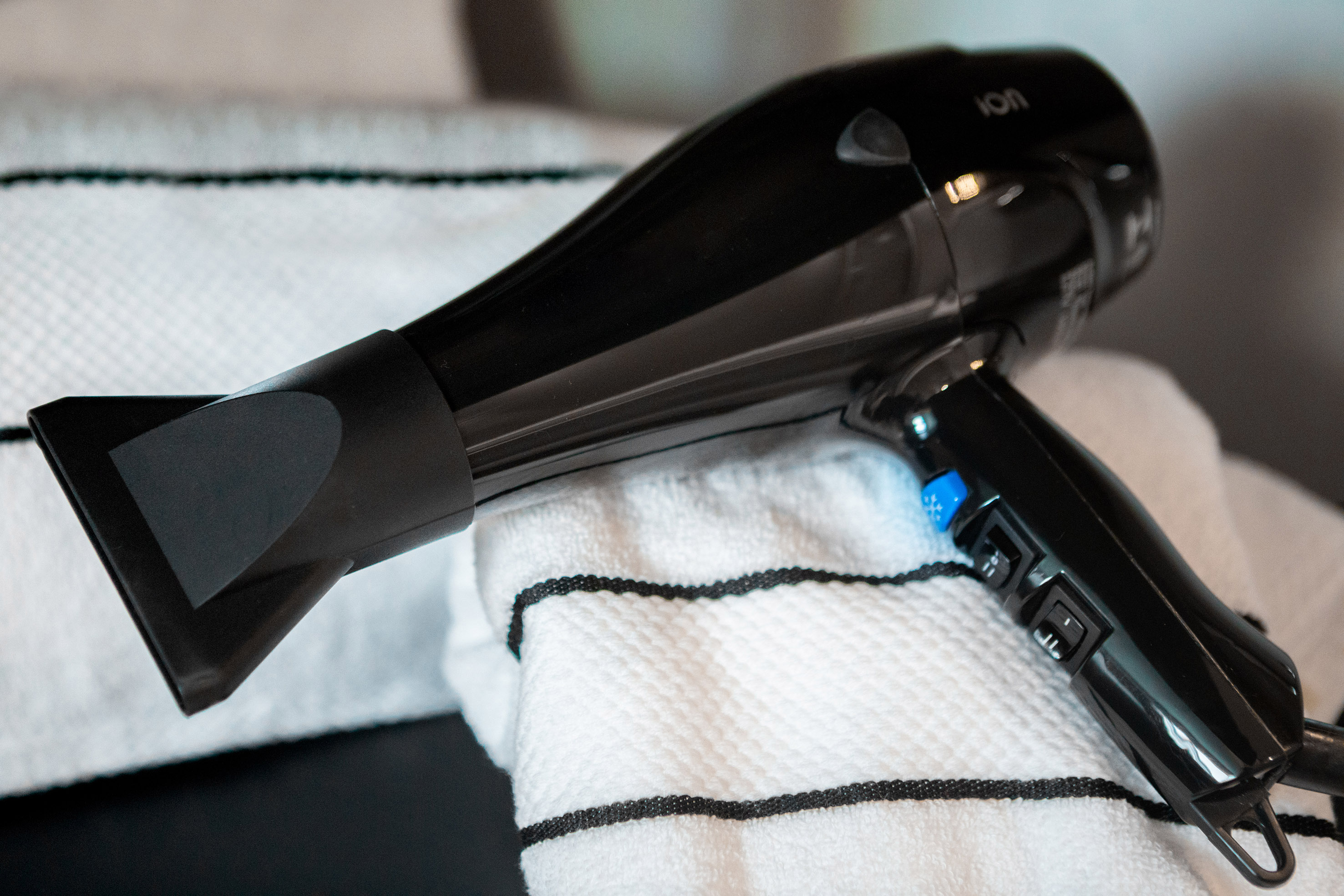Black hair dryer with blue button on a striped white towel.