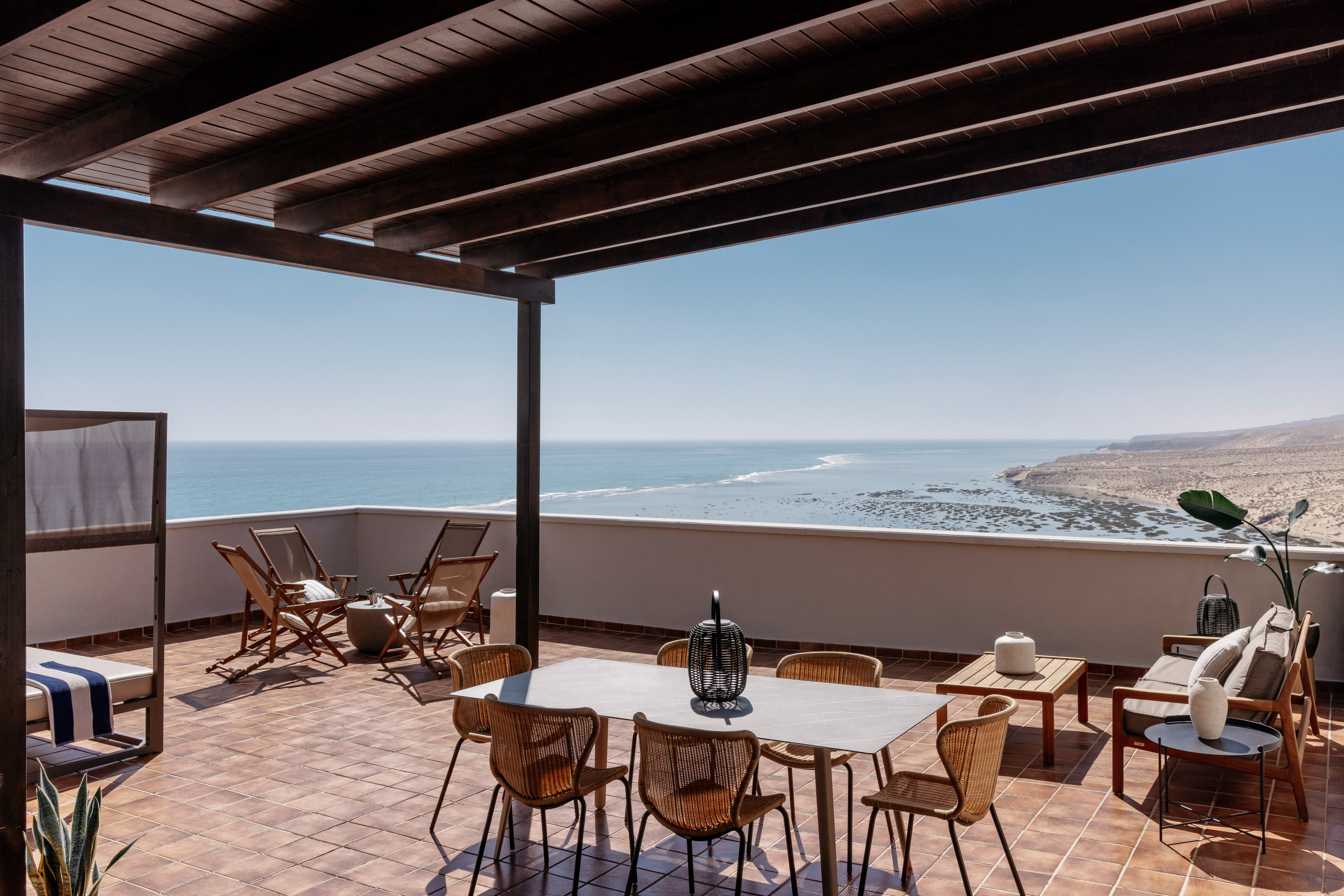 Ocean view terrace with outdoor dining, lounge, pergola, and desert coastline.