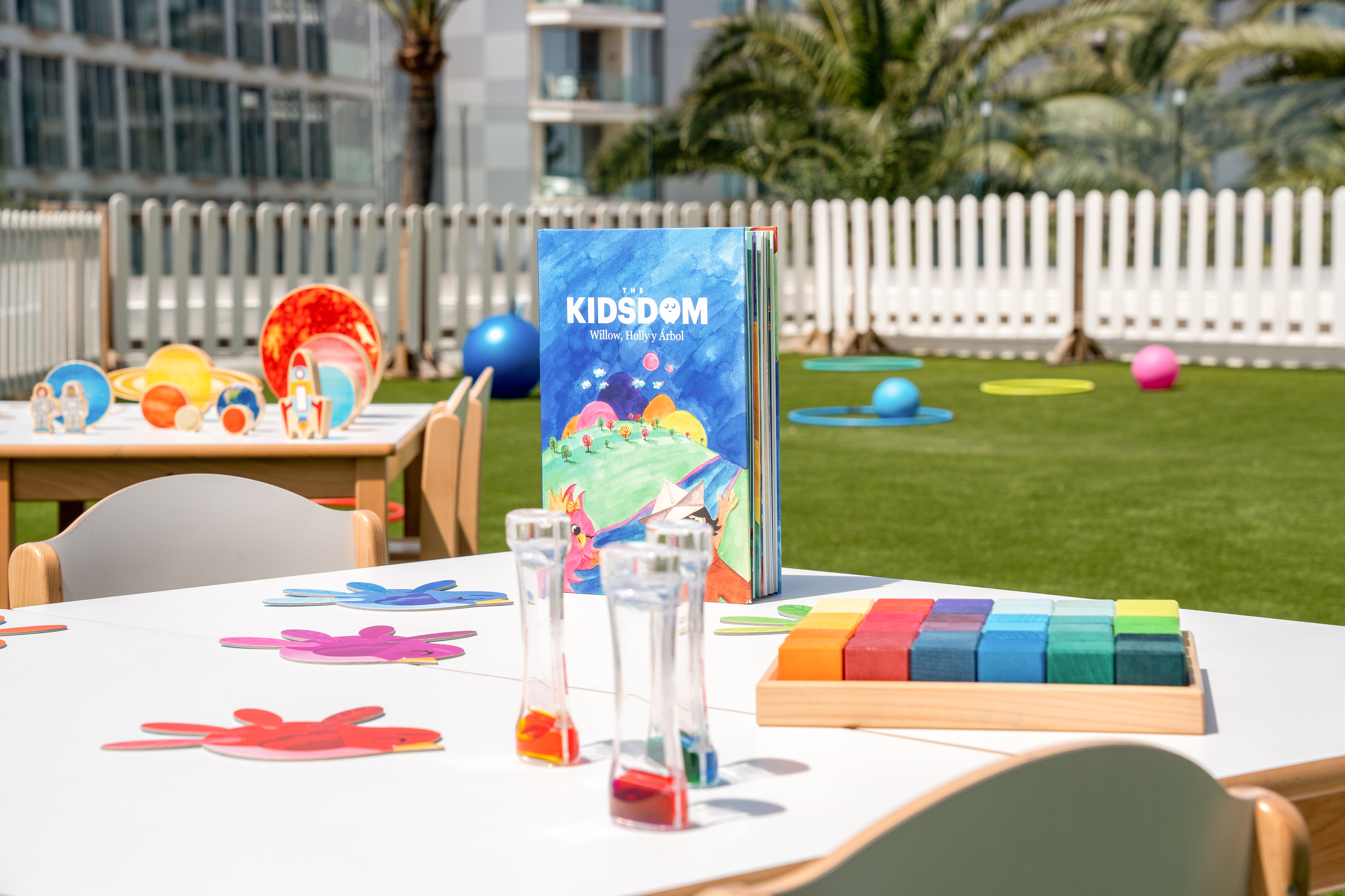 Vibrant outdoor kids club play area with "The KIDSDOM" book and learning toys.