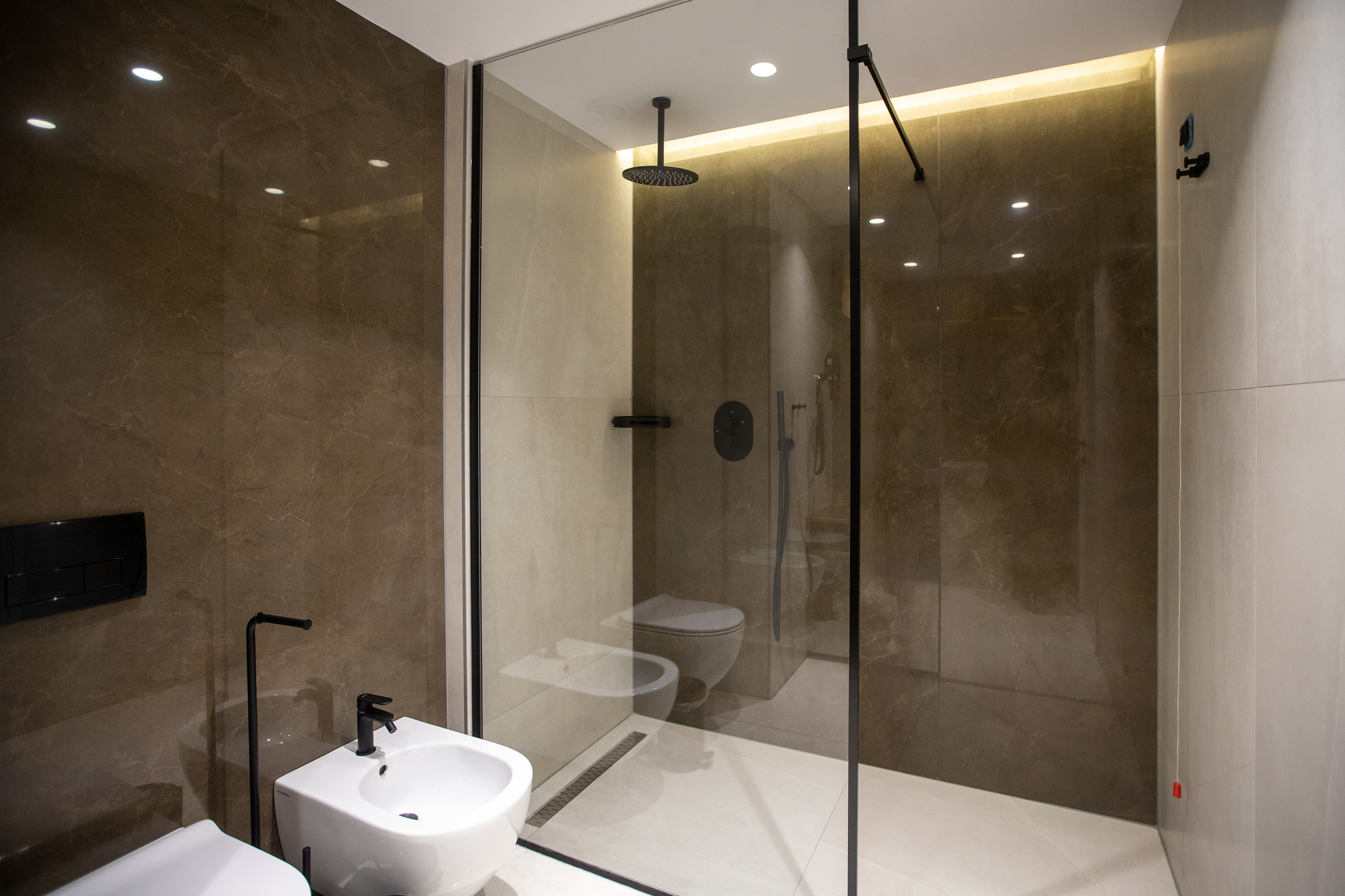 Modern glass shower with rain head in a bathroom with dark marble walls.