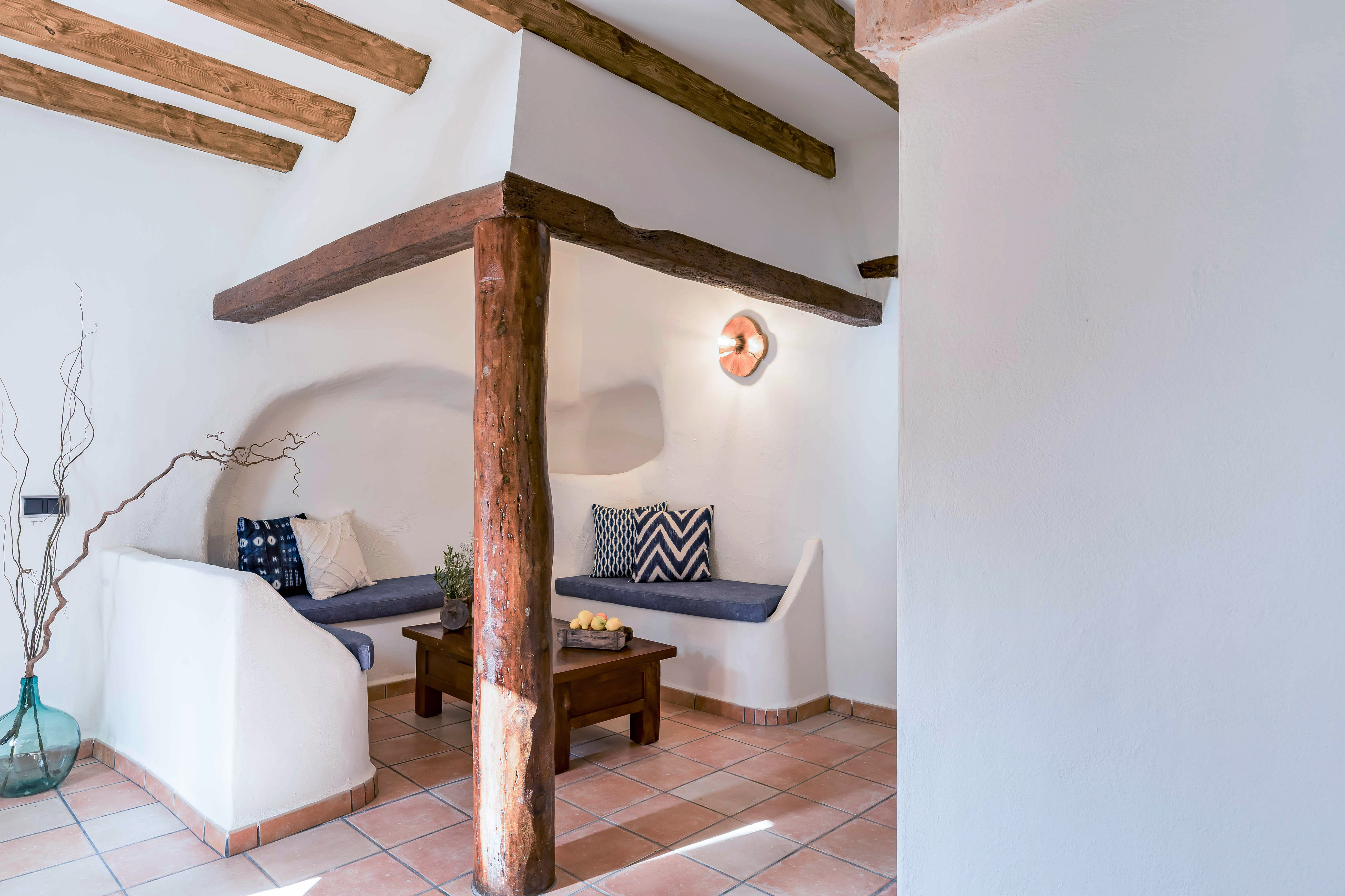 Cozy rustic room with white walls, wooden beams, built-in seating, terracotta floor.