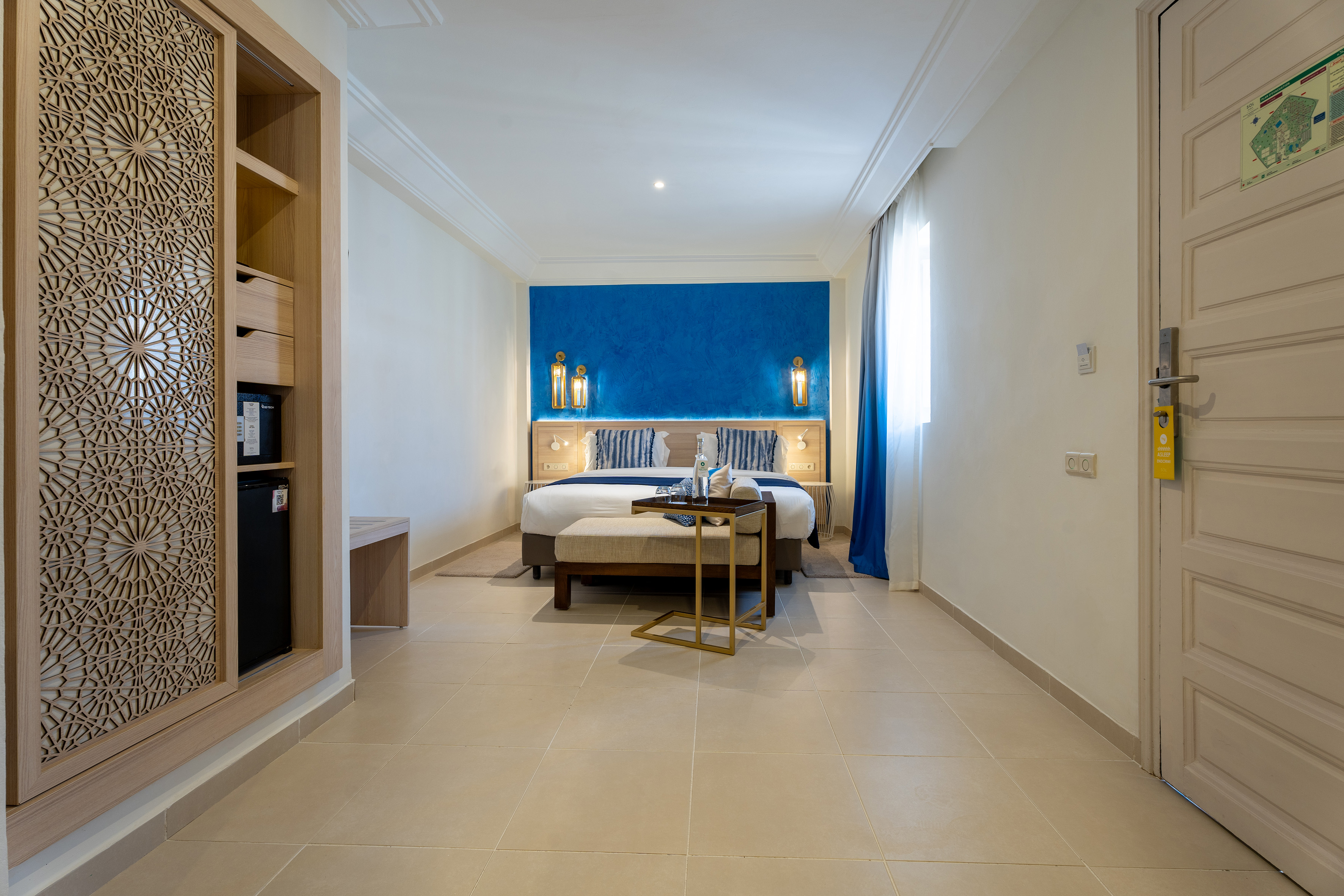 Modern hotel bedroom with blue accent wall, bed, and intricate carved wardrobe. - Sol Room - SOL Oasis Marrakech, Marrakech