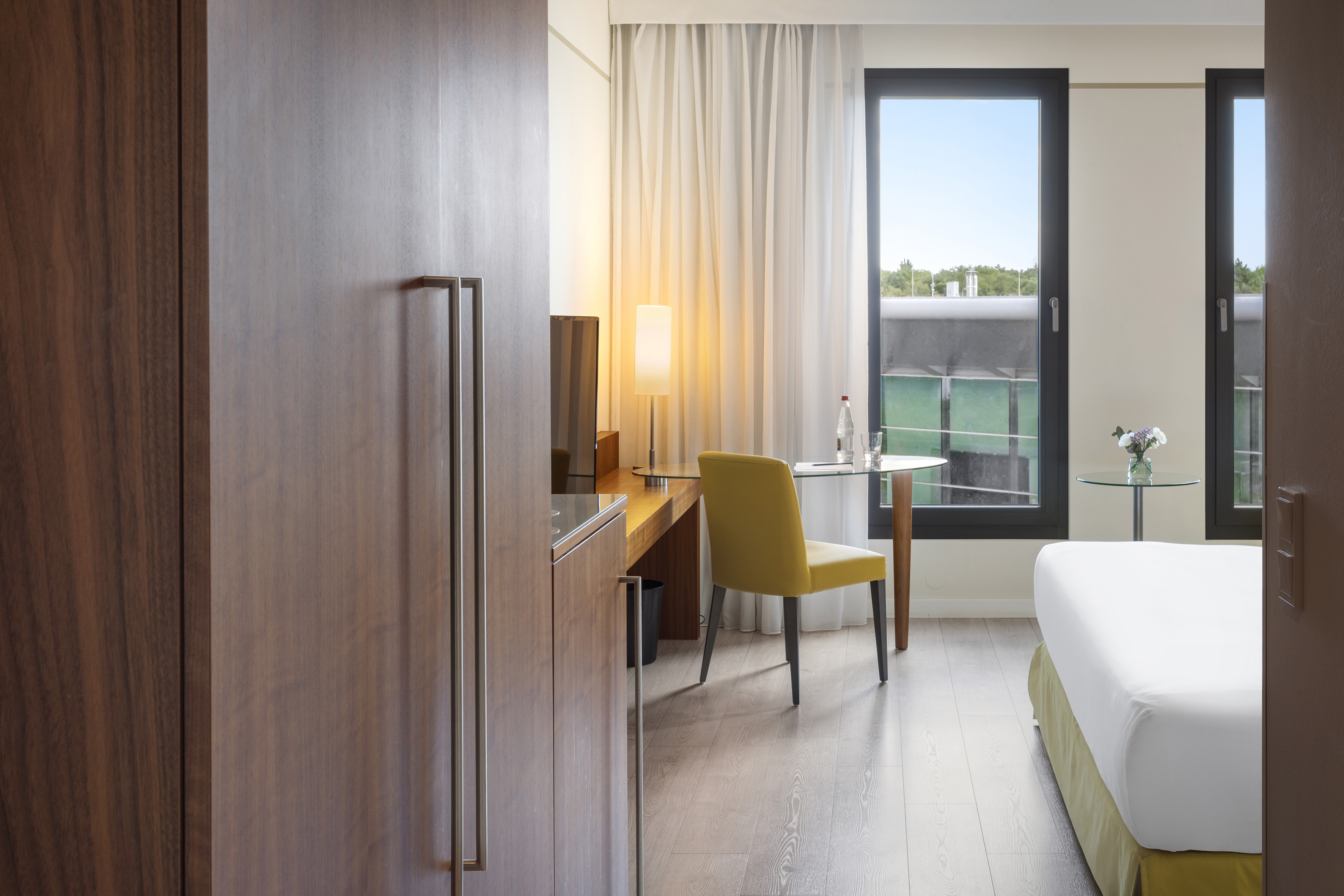 Modern hotel room with desk, yellow accent chair, and built-in wooden closet.