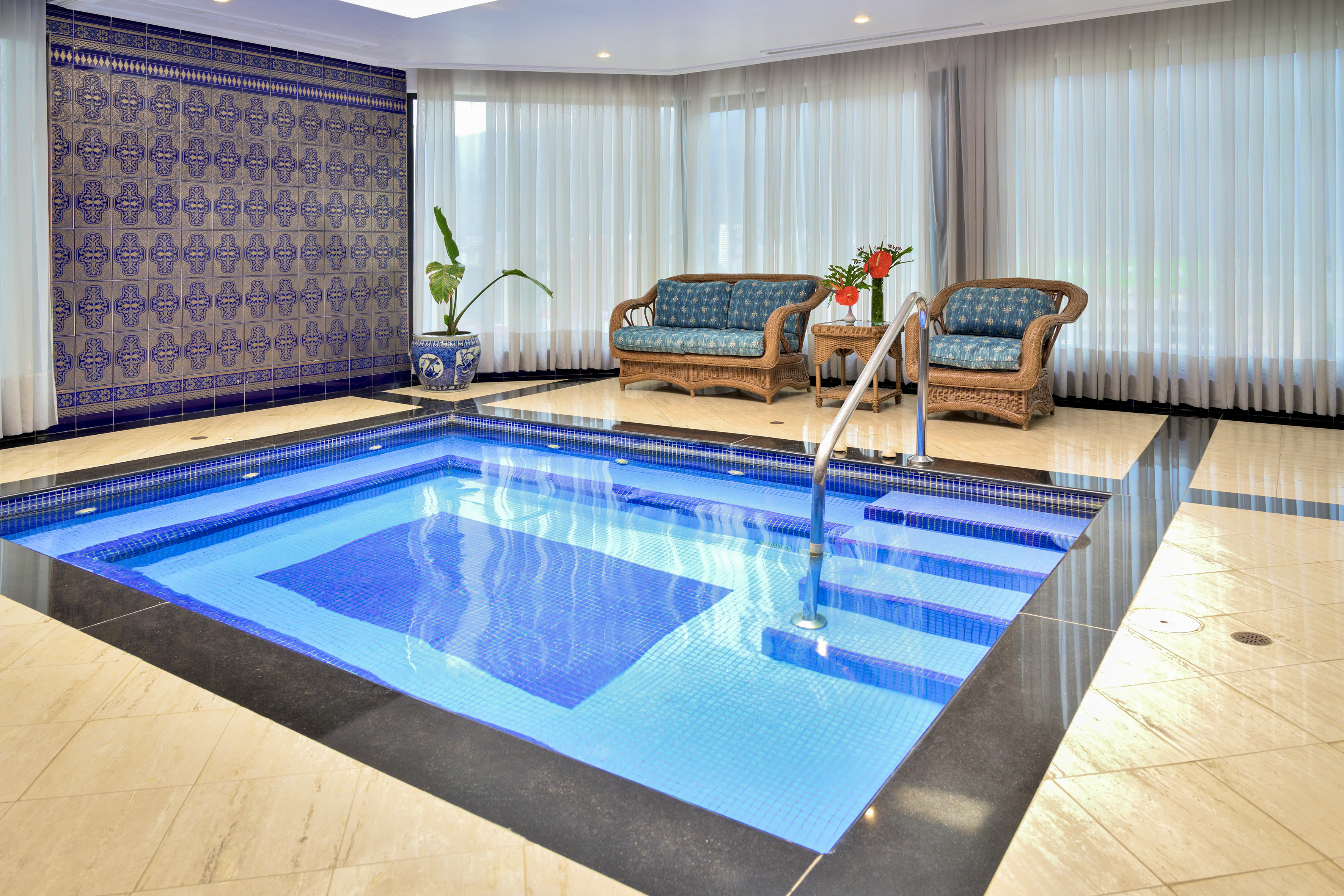 Indoor plunge pool with blue mosaic tiles, ornate wall, and wicker seating.