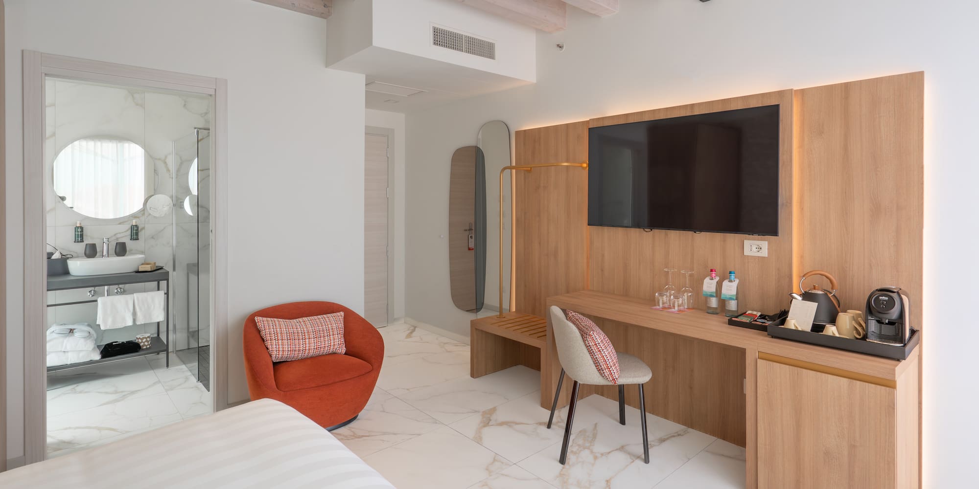 Modern hotel room interior with marble floor, wooden TV wall, and bright bathroom.