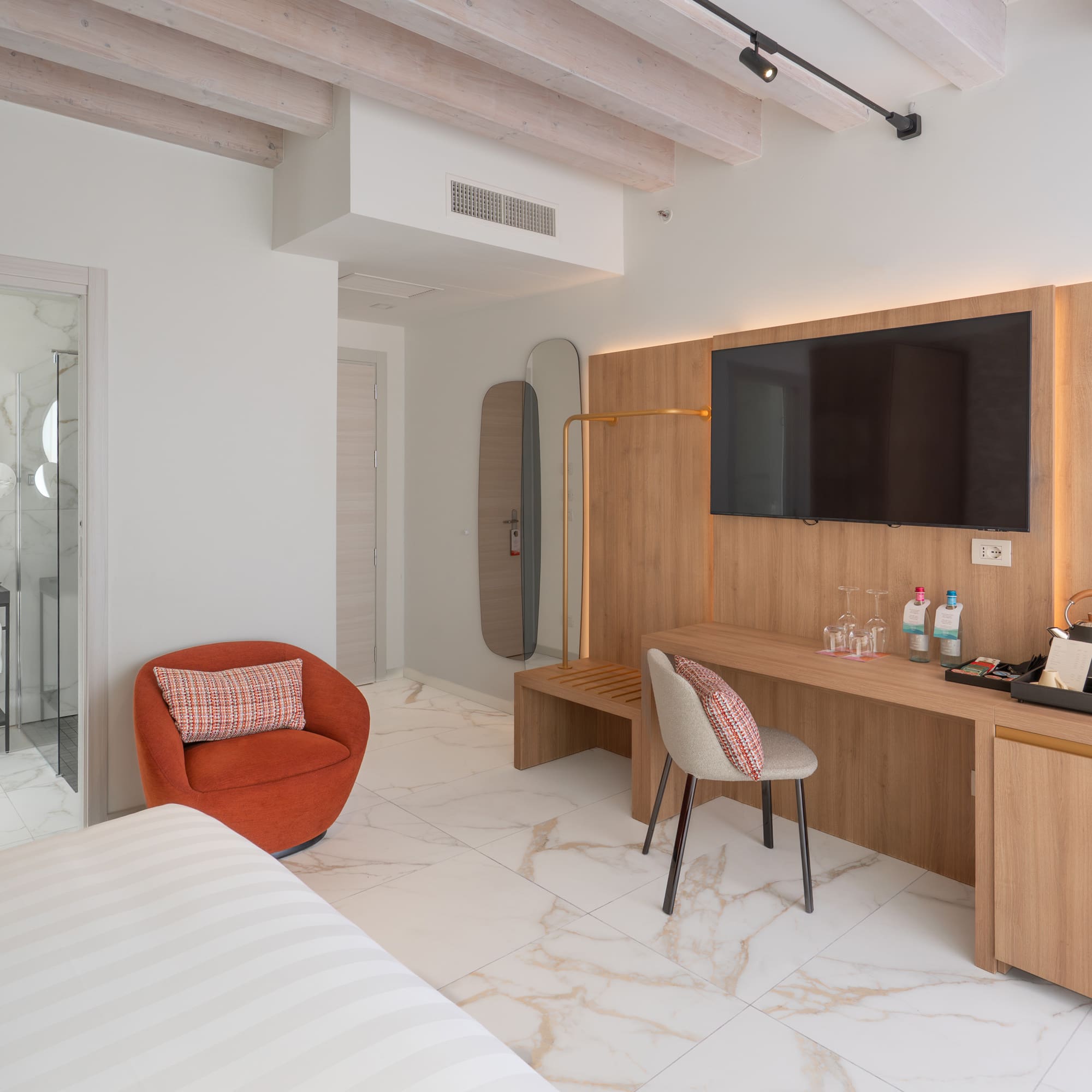 Modern hotel room interior with marble floor, wooden TV wall, and bright bathroom.