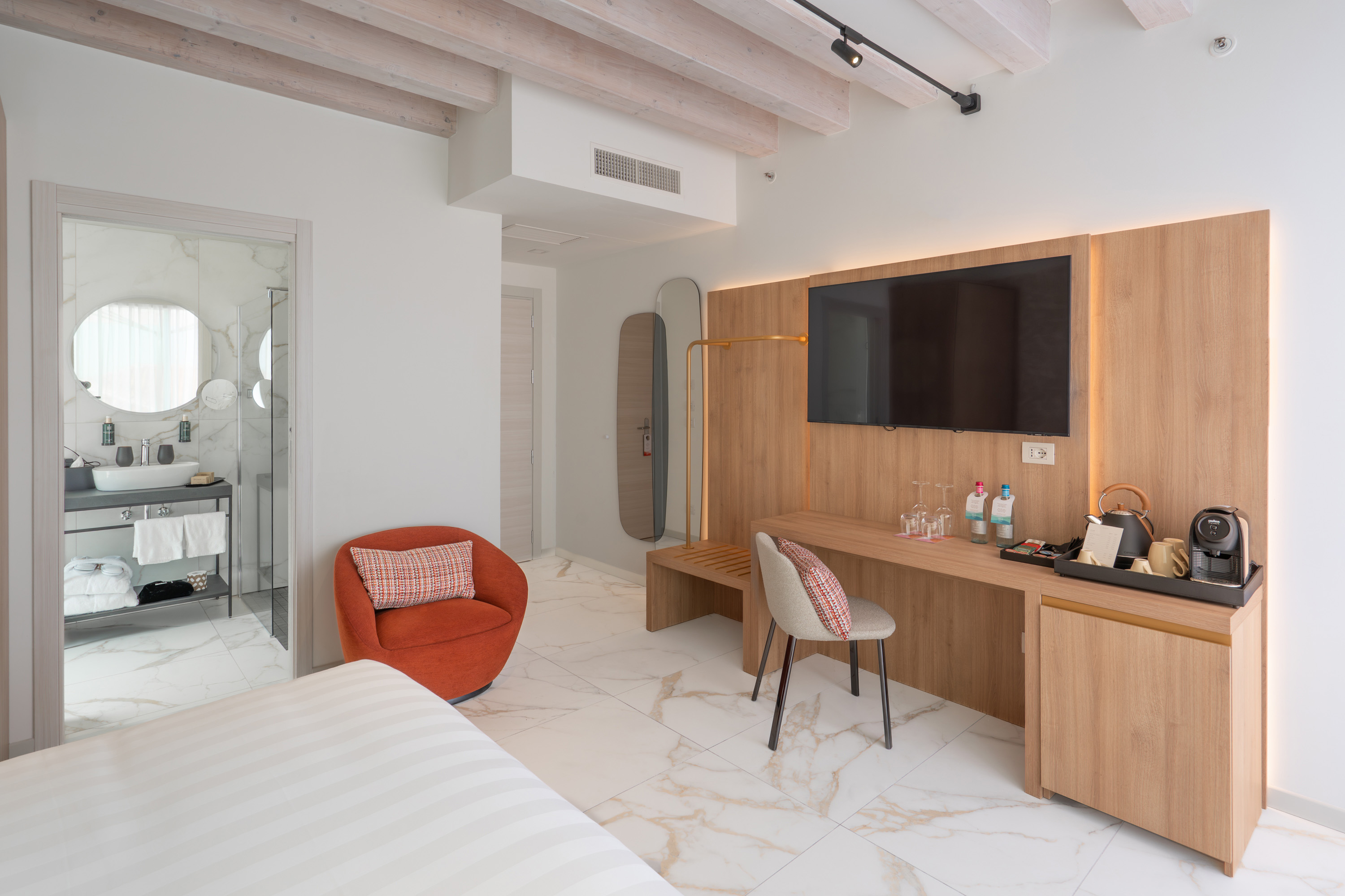 Modern hotel room interior with marble floor, wooden TV wall, and bright bathroom.