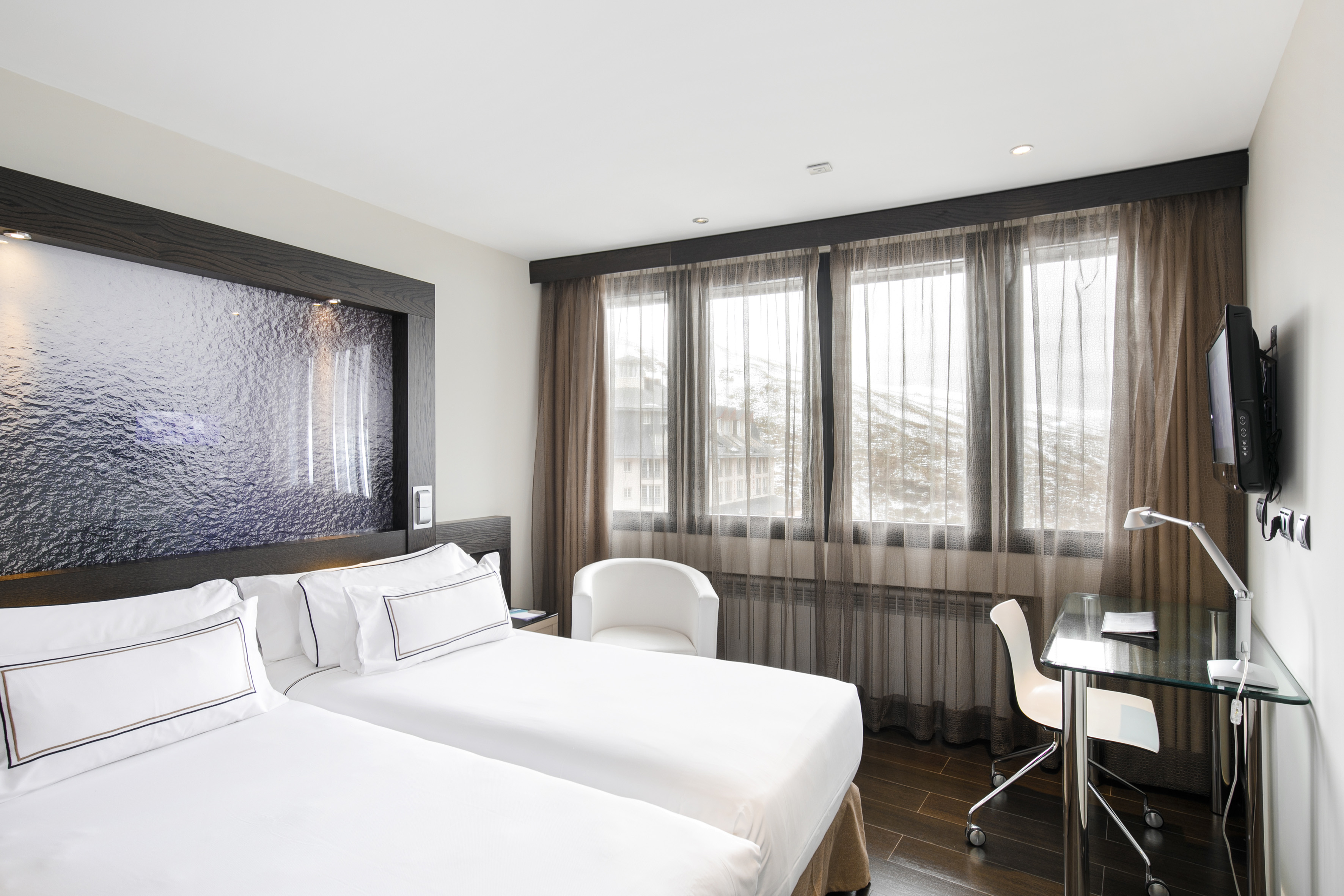Modern hotel room with twin beds, desk, and snowy mountain view.