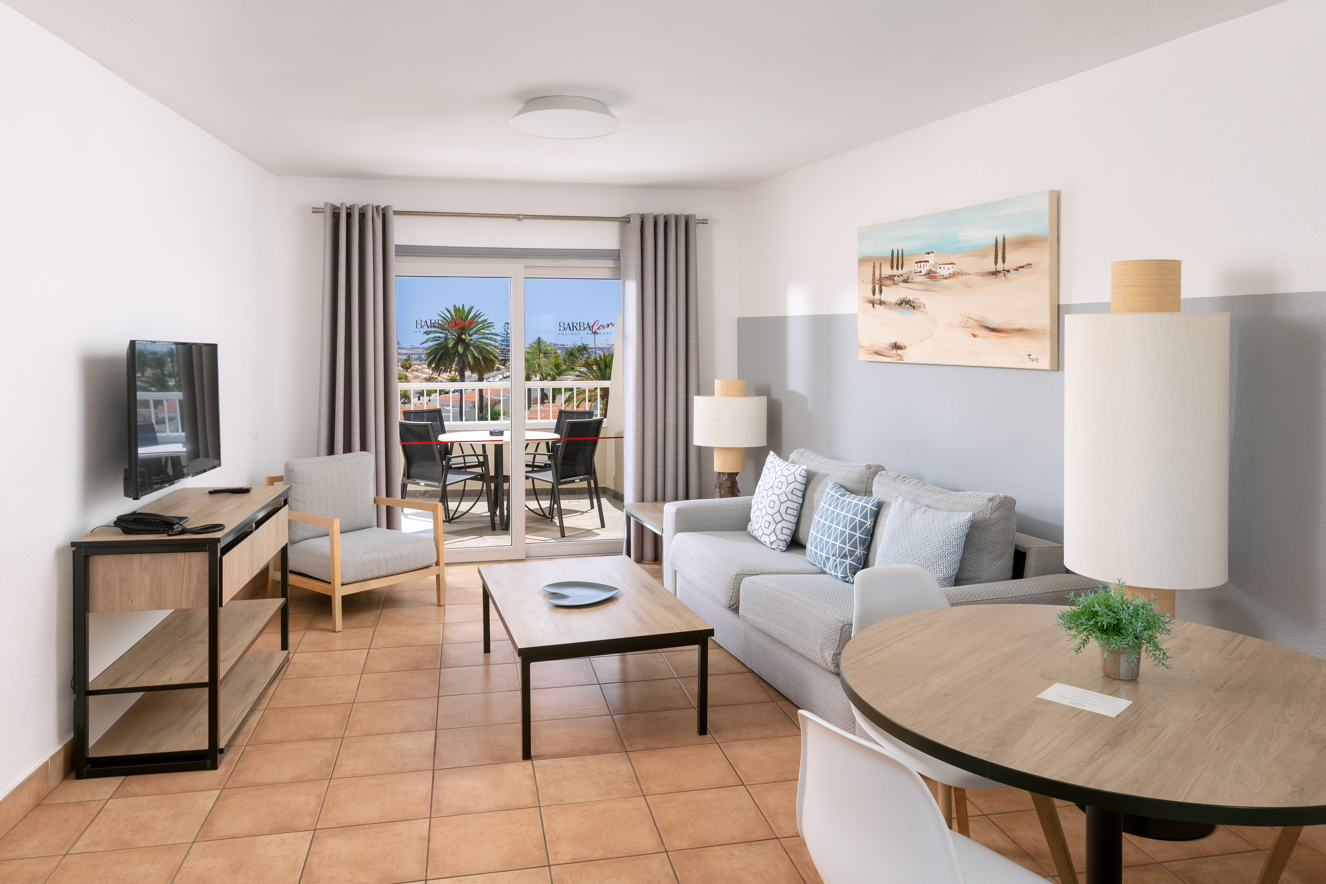 Stylish apartment living room with sofa, TV, dining, and balcony with palm trees.