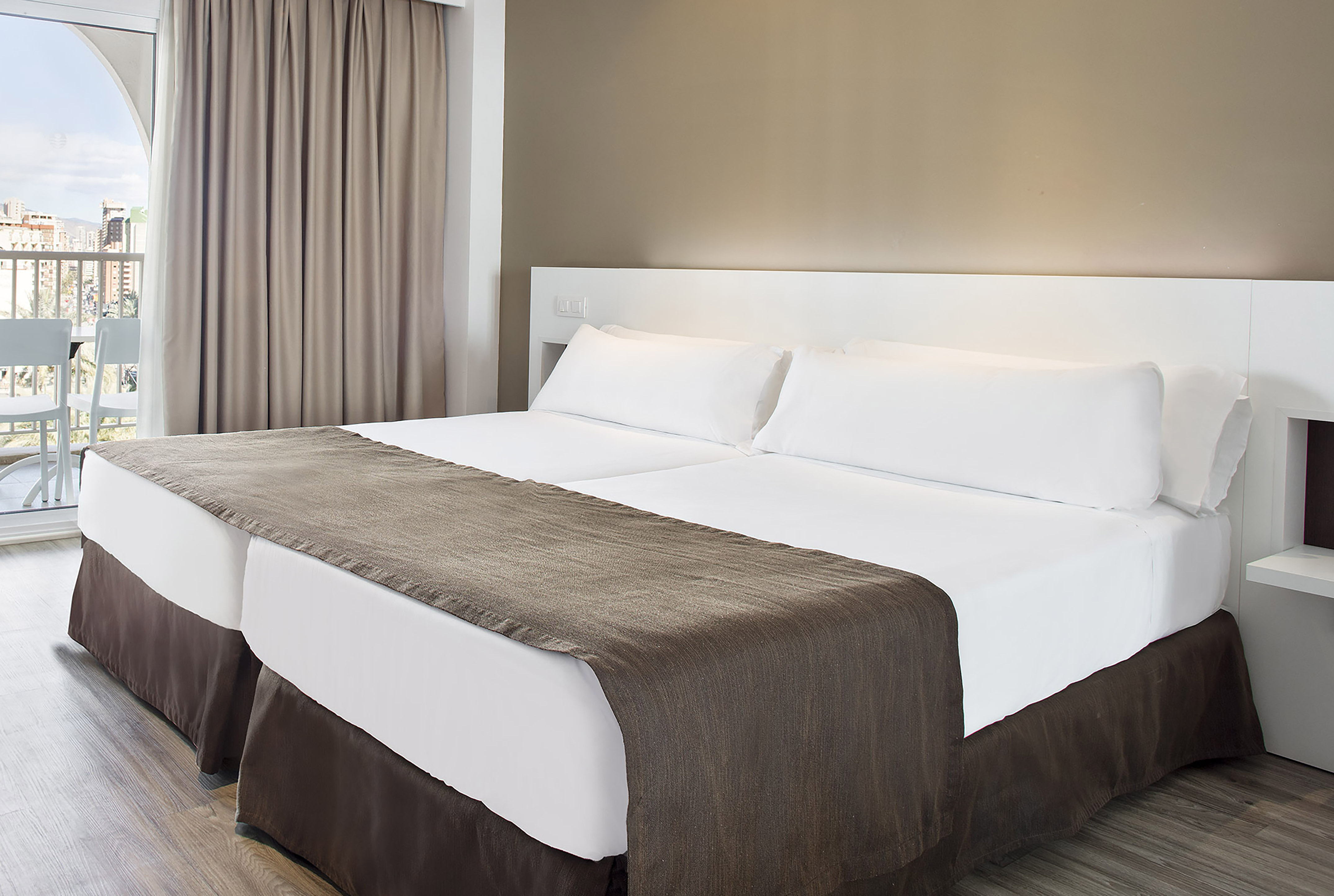Comfortable hotel room with twin beds, white bedding, and city view balcony.