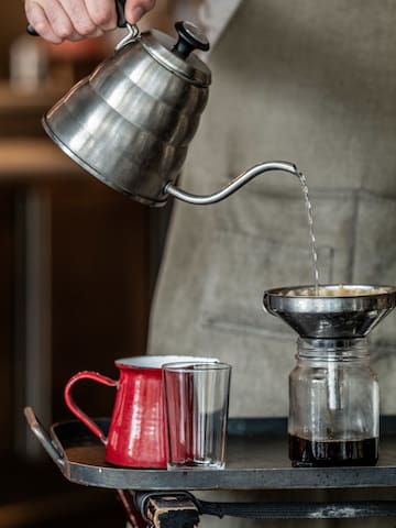 a metal kettle pouring liquid into a glass