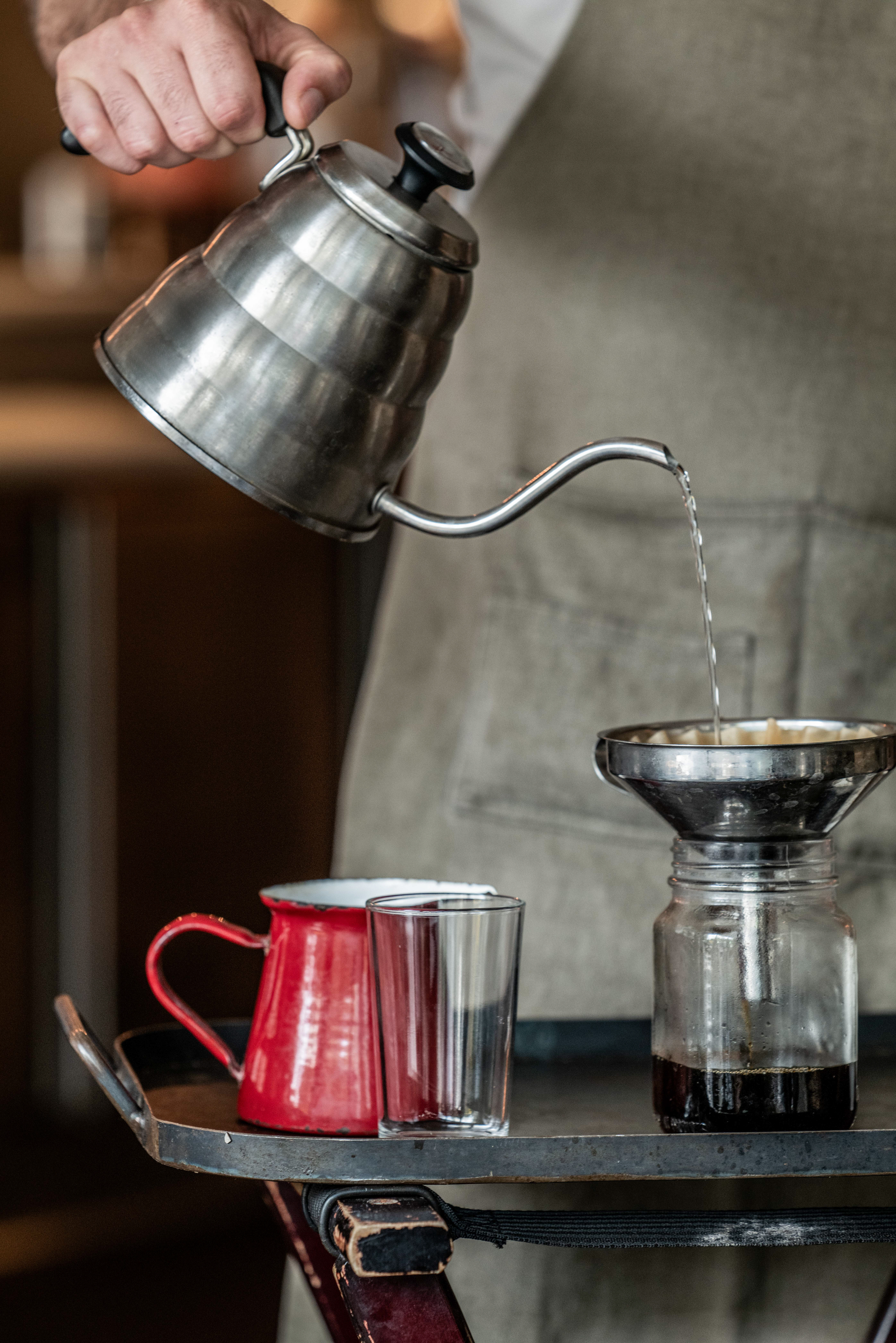 a metal kettle pouring liquid into a glass