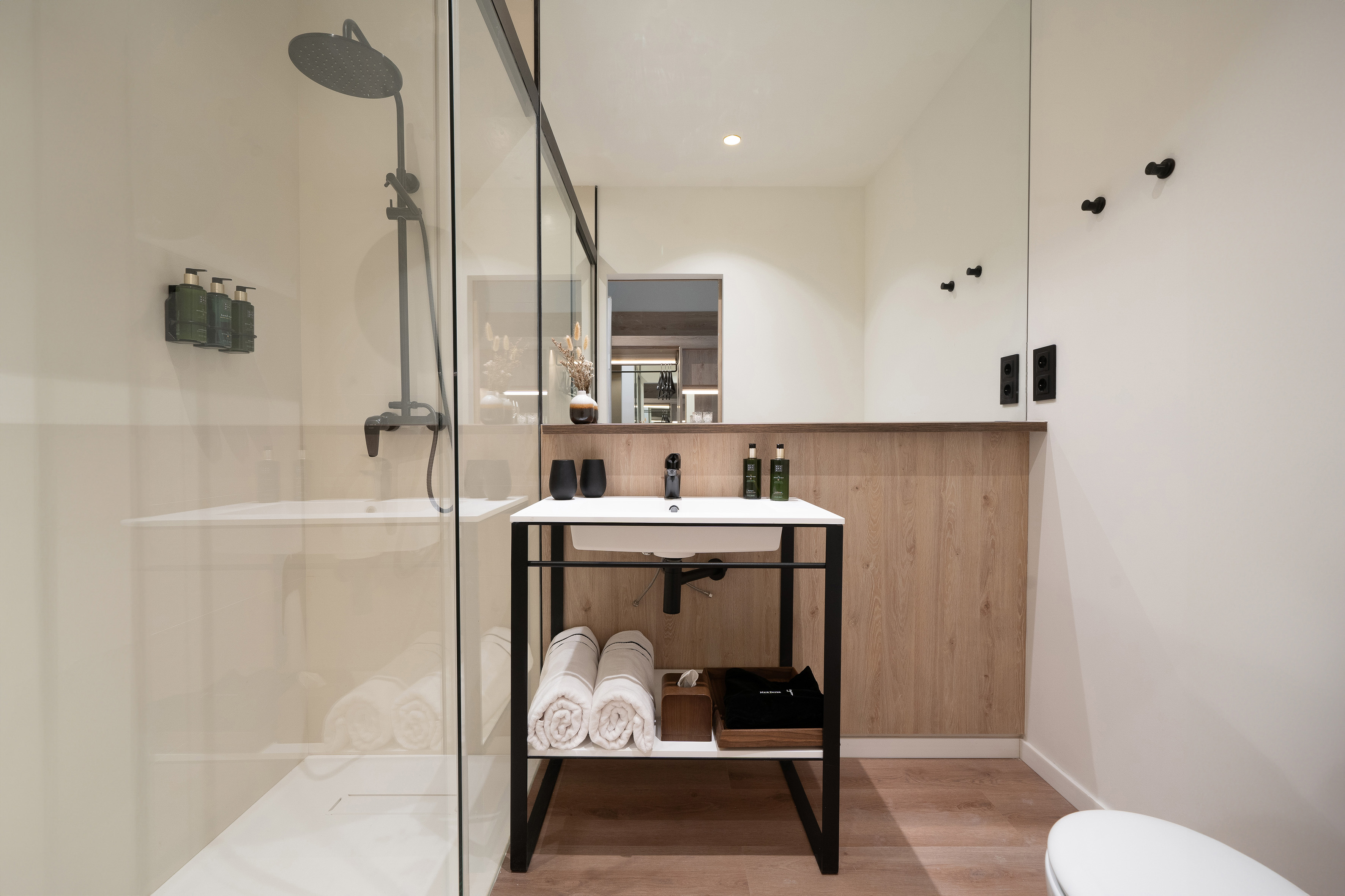 Sleek modern hotel bathroom with glass shower, white vanity, and wood accents.