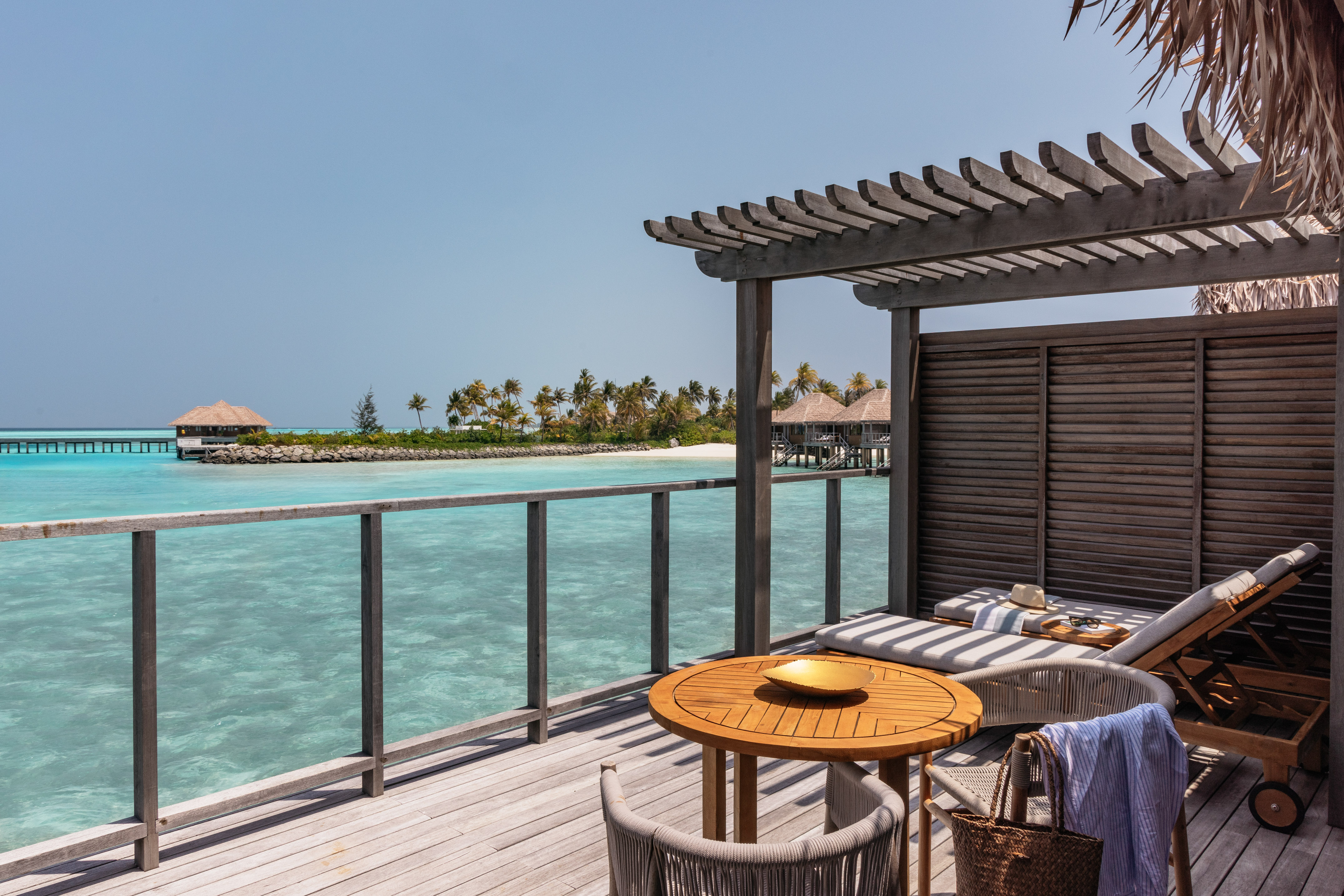 Maldives overwater bungalow deck with turquoise sea, palm trees, and resort view.