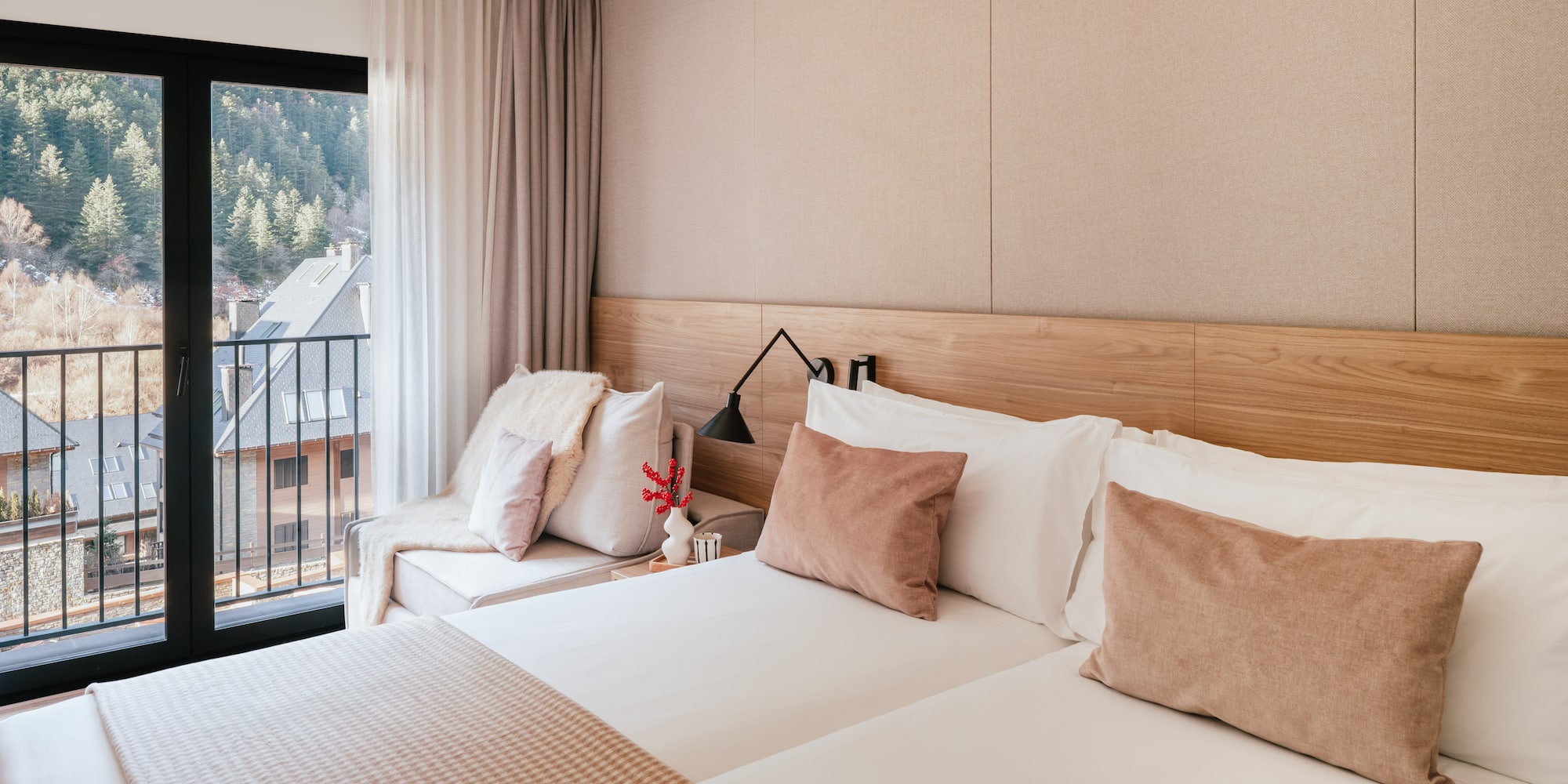 Modern hotel room with mountain view balcony and neutral wooden decor.