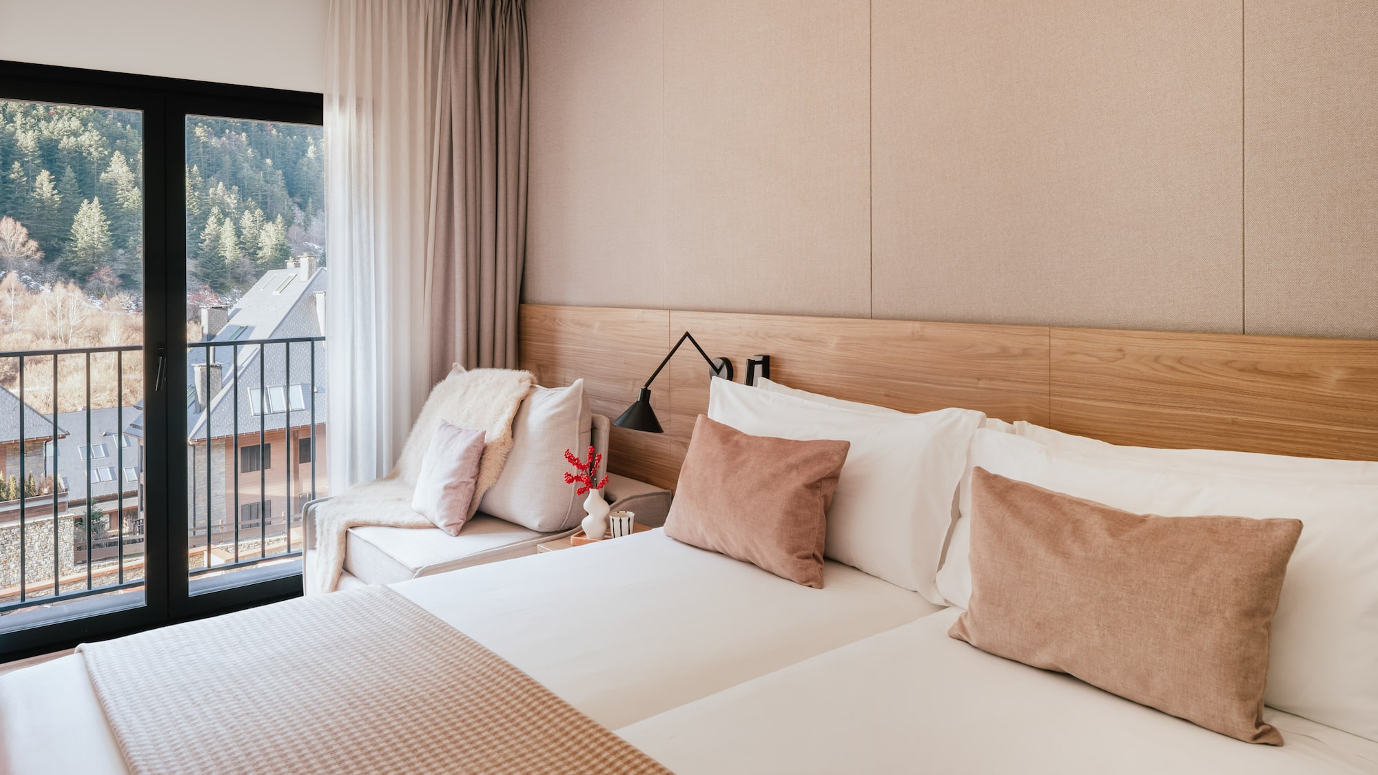 Modern hotel room with mountain view balcony and neutral wooden decor.