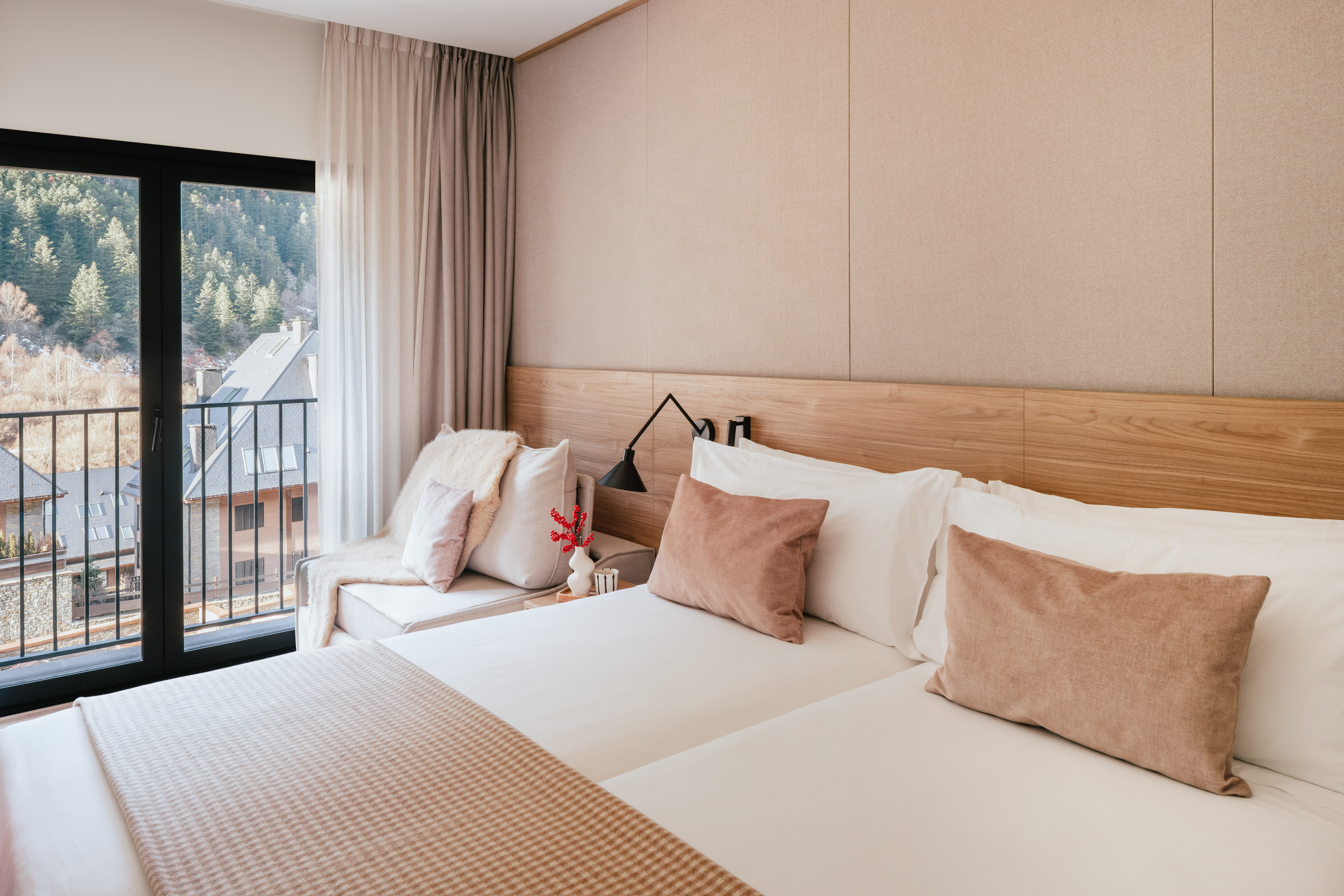 Modern hotel room with mountain view balcony and neutral wooden decor.