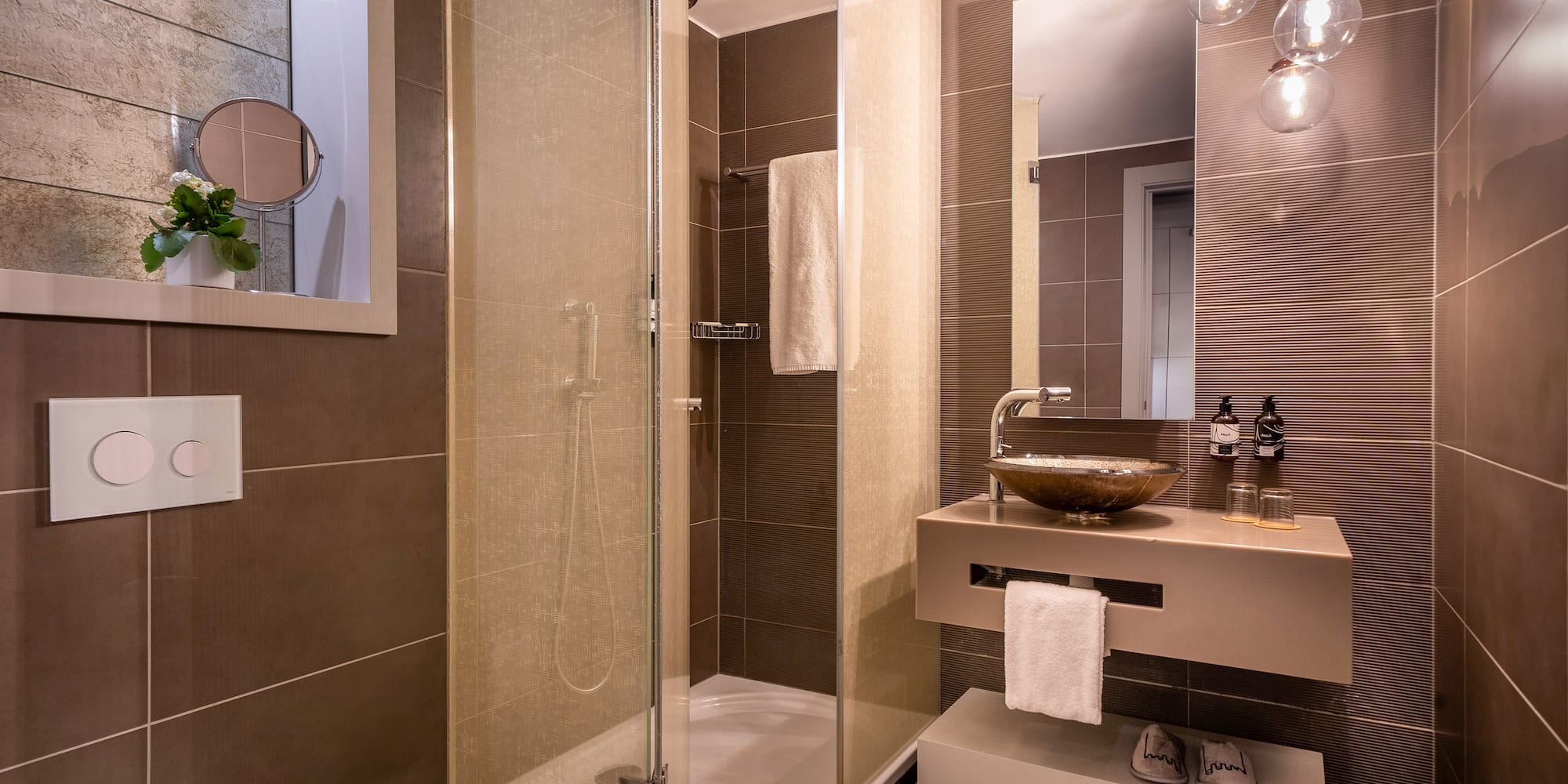 Modern brown-tiled bathroom with glass shower, floating vanity, and mirror.