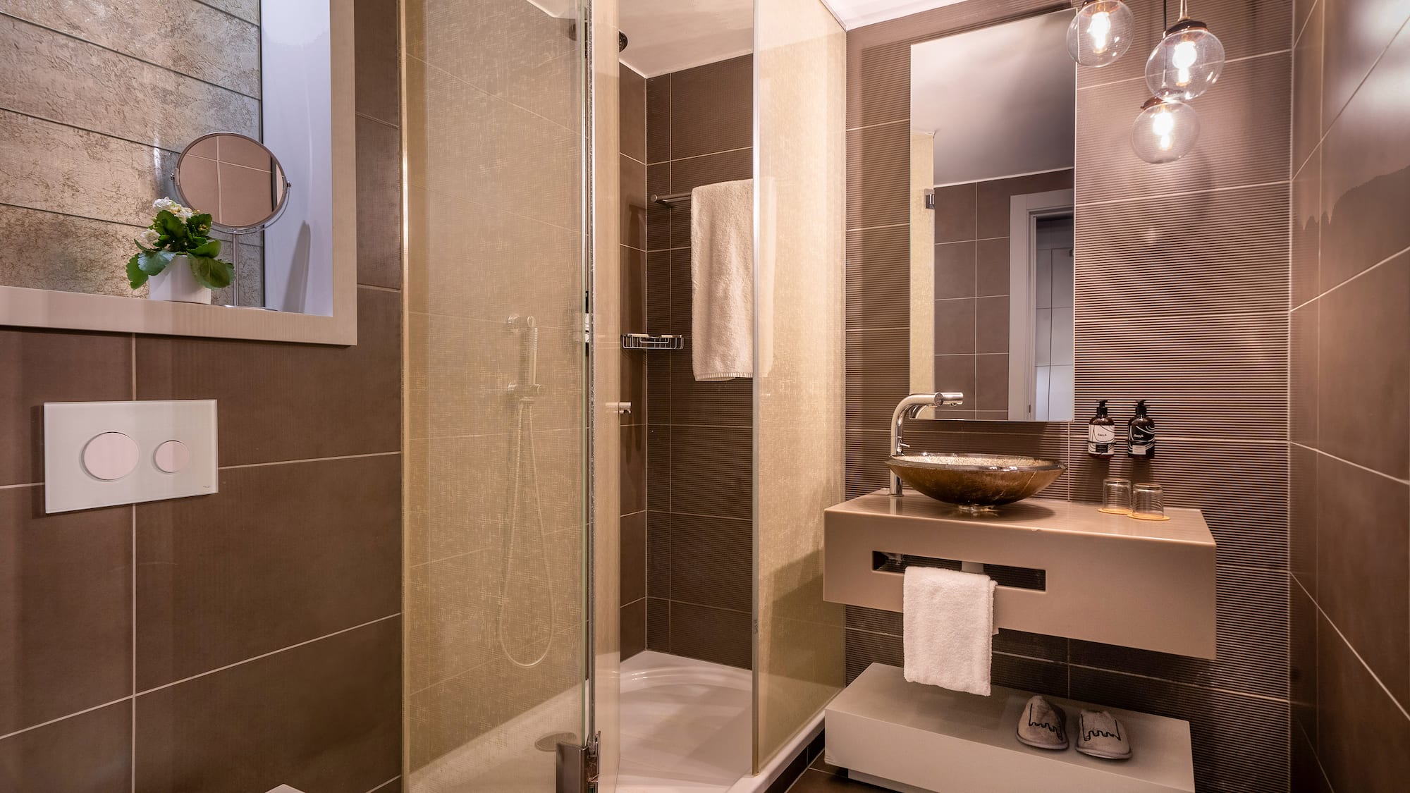 Modern brown-tiled bathroom with glass shower, floating vanity, and mirror.