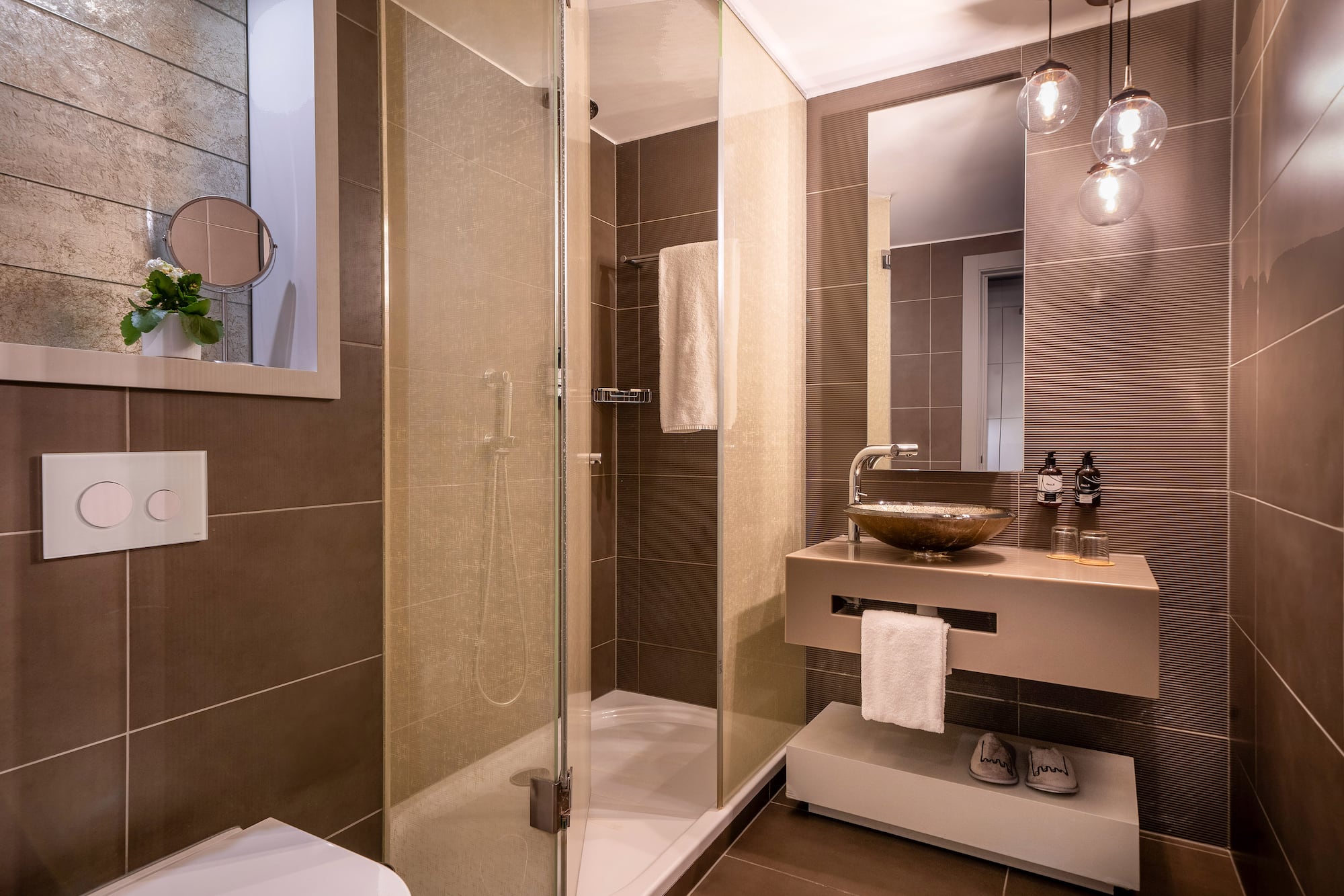 Modern brown-tiled bathroom with glass shower, floating vanity, and mirror.